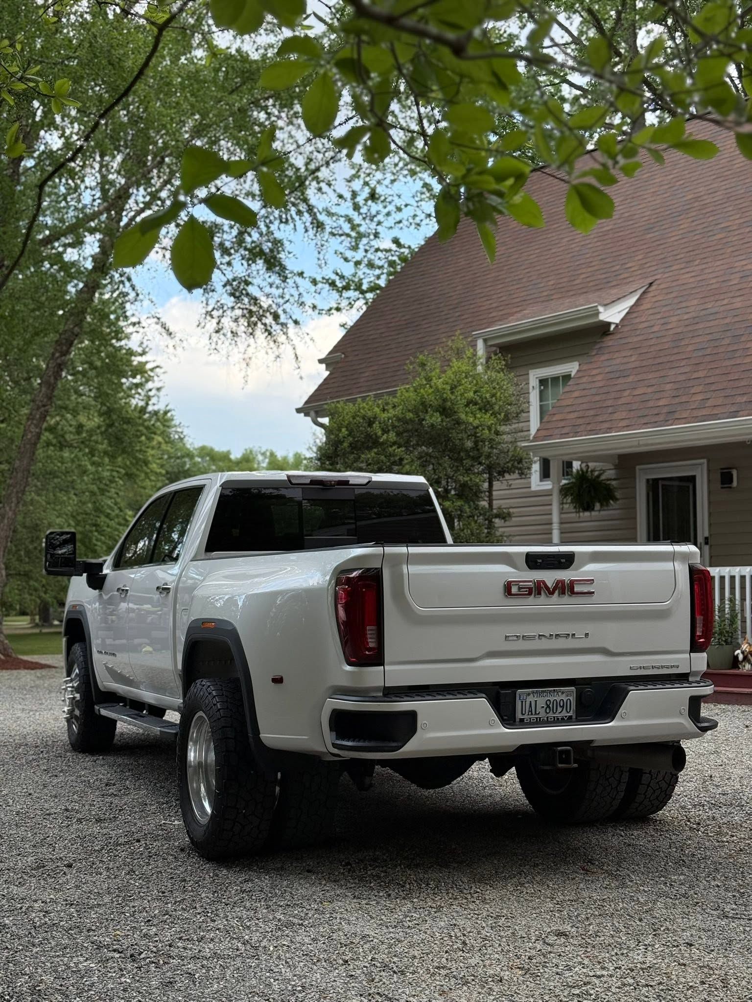 White GMC pickup truck parked on a gravel driveway beside a house under leafy trees