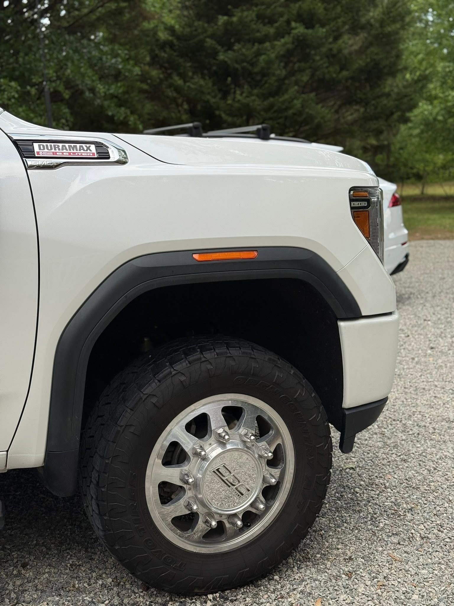 White pickup truck front wheel and fender on a gravel road with trees in the background
