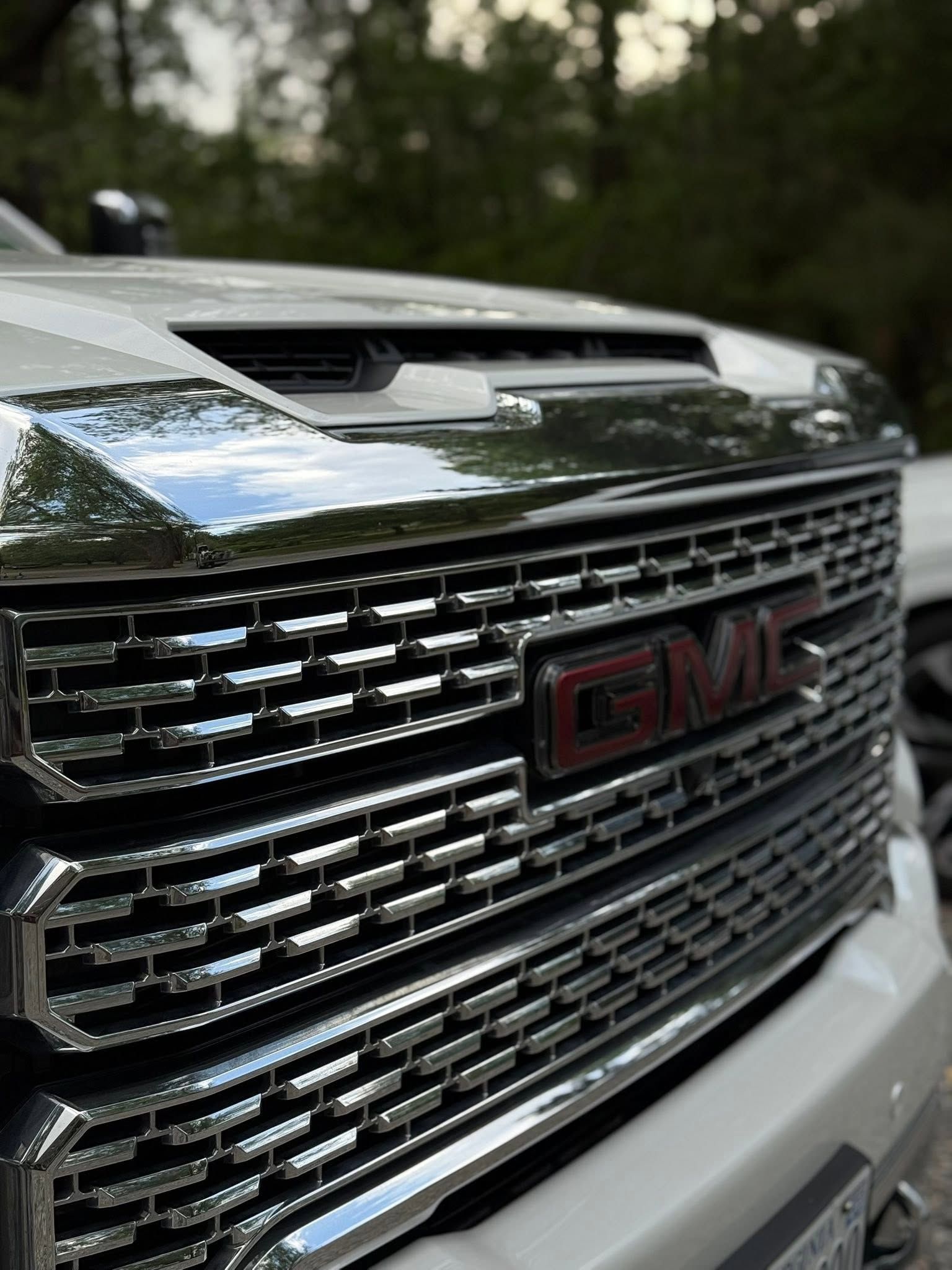 Close-up of a chrome GMC truck grille with red logo and hood scoop