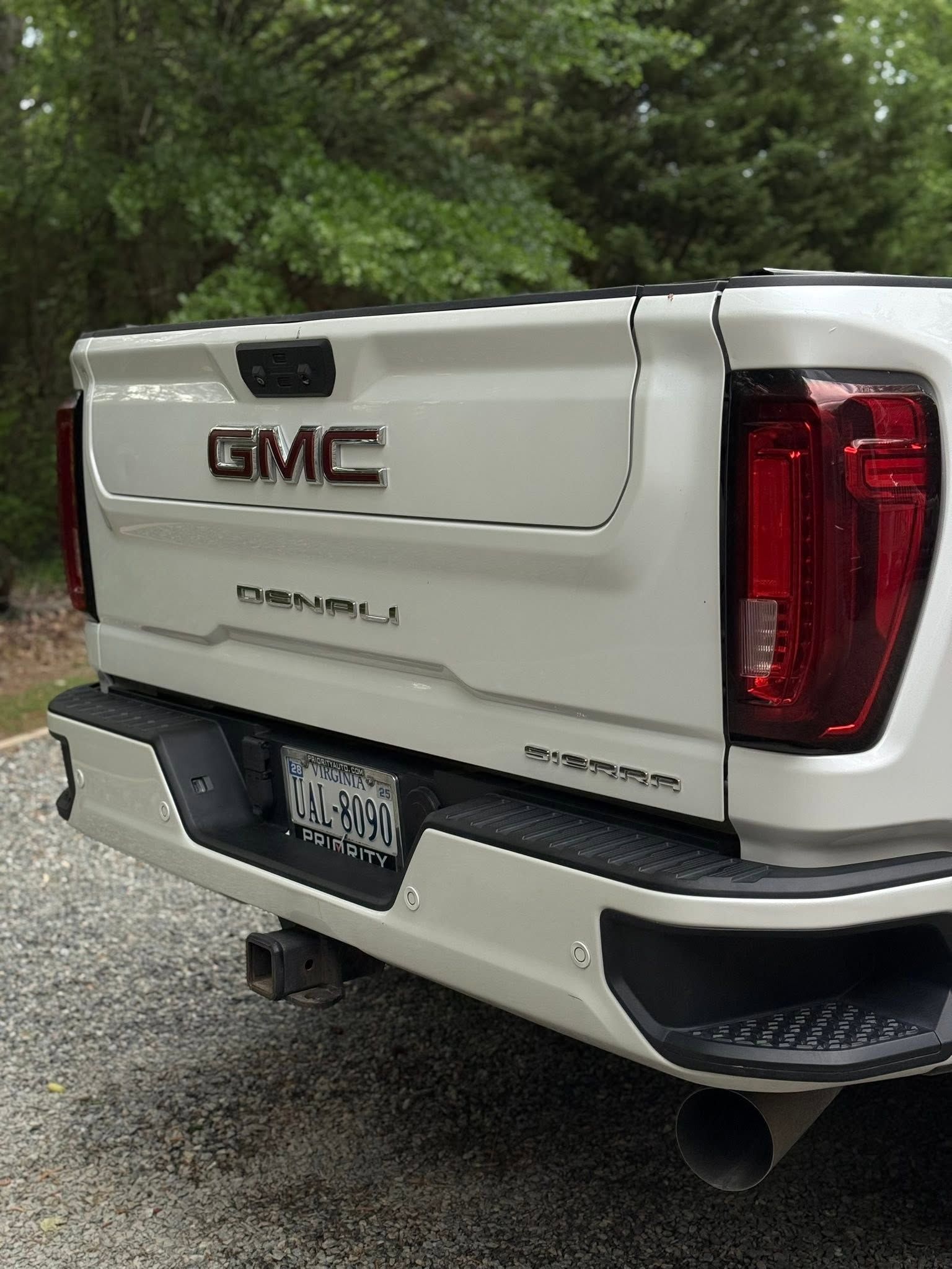 White GMC Sierra Denali tailgate and rear bumper parked on a gravel road beside trees
