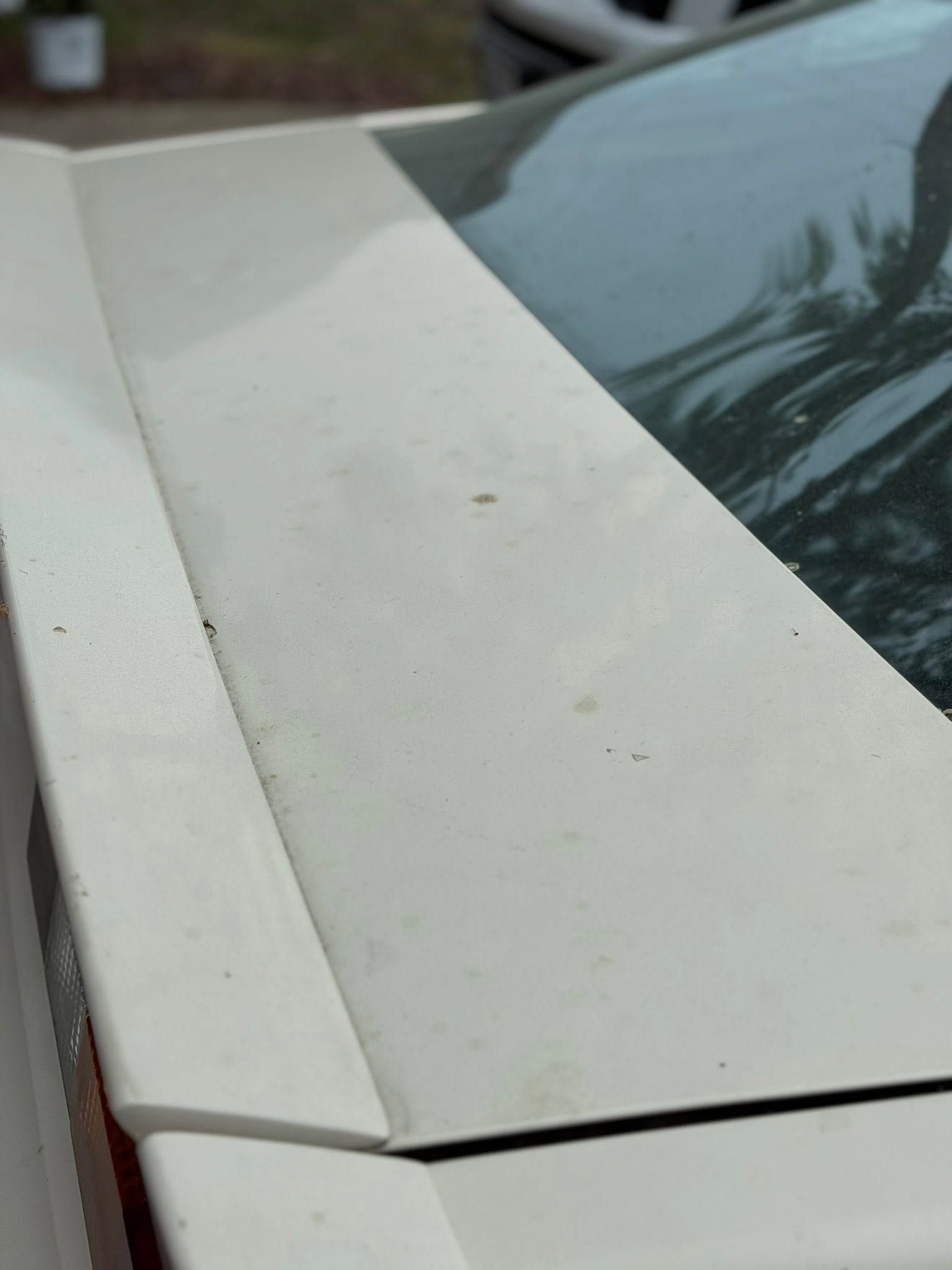 Close-up of a white car hood with a small crack near the edge, beside a dark windshield.