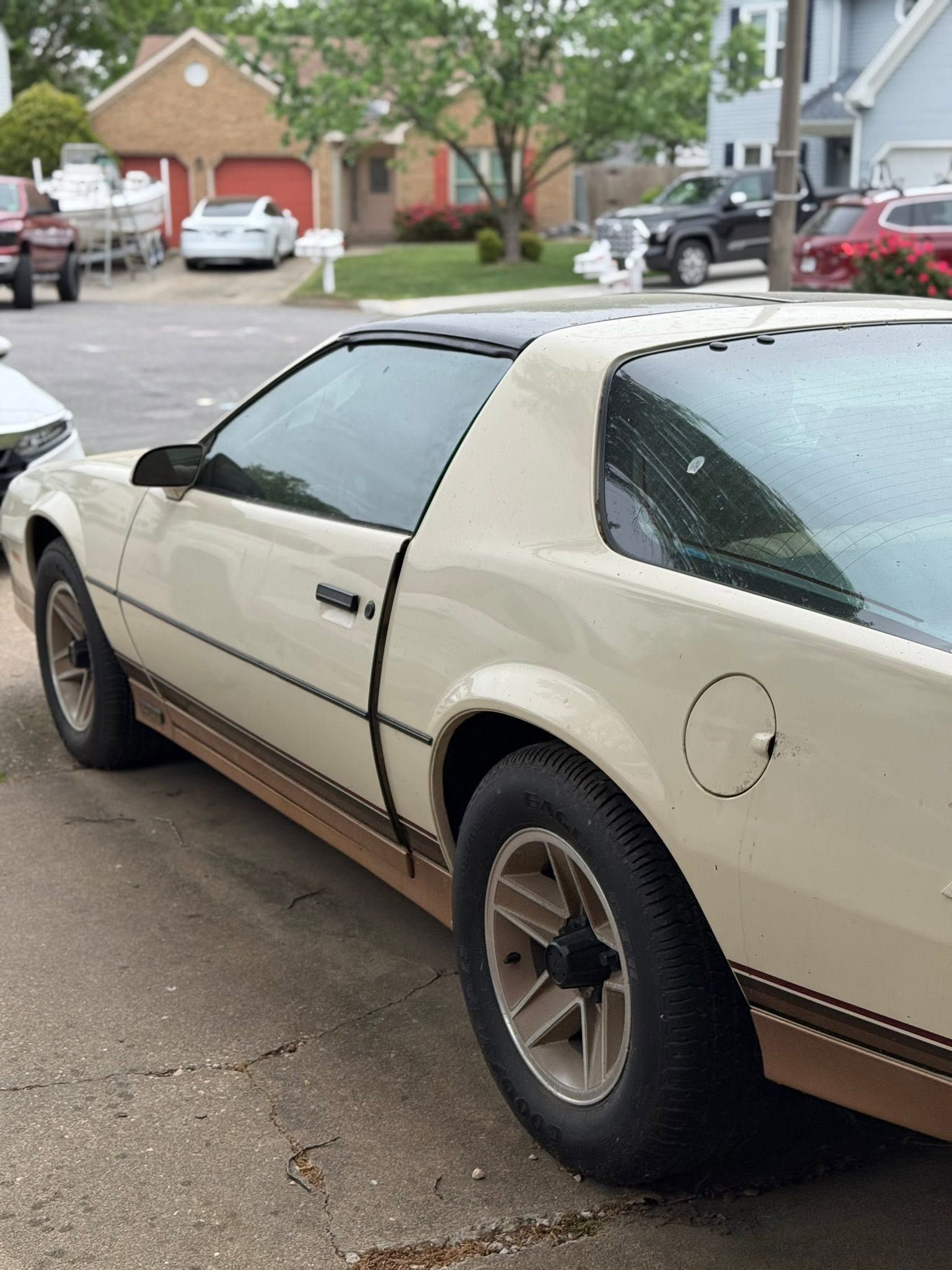 Beige sports car parked on a residential street with brick houses in the background