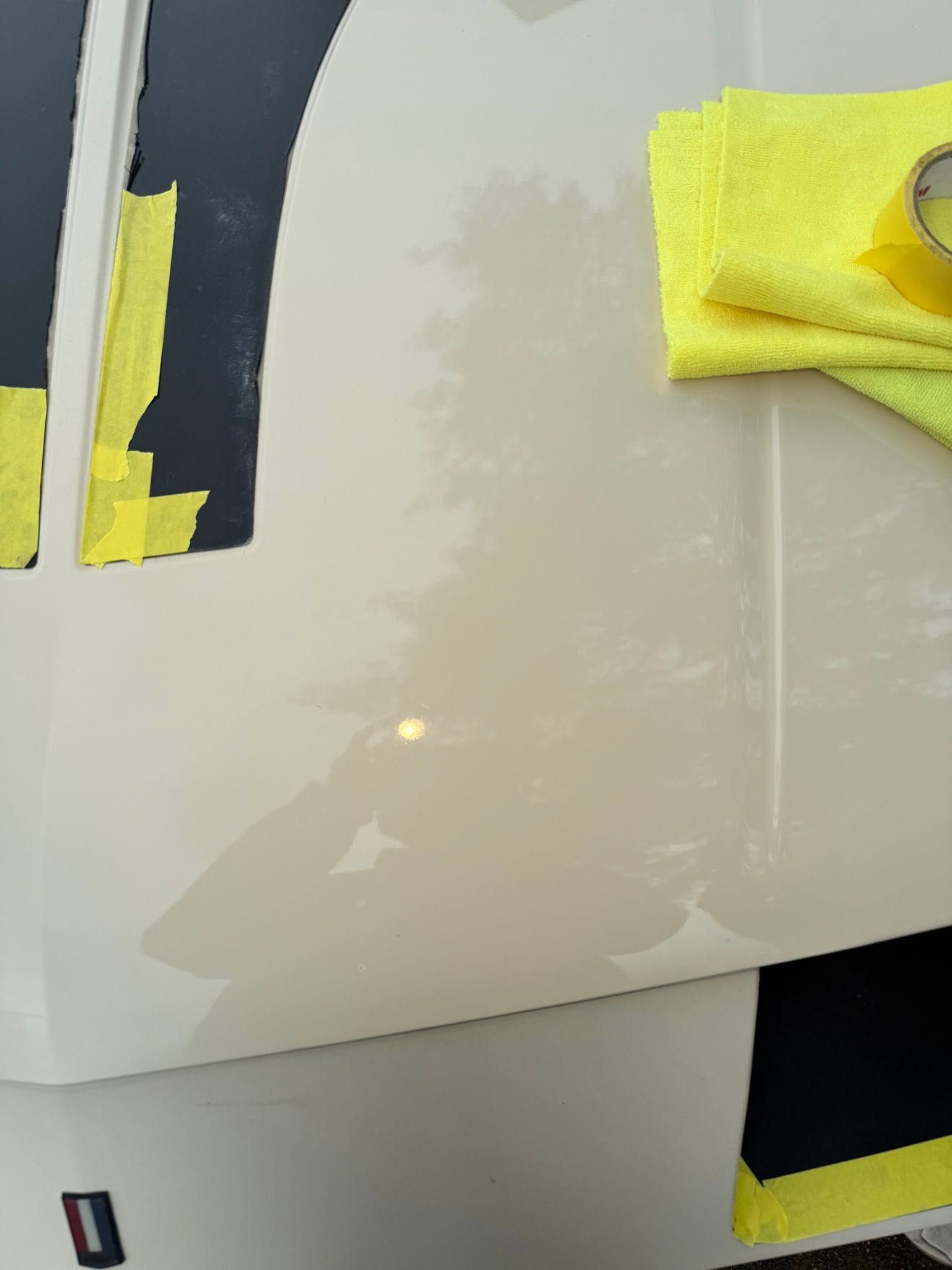 Glossy white car panel with yellow masking tape and black trim during paint work