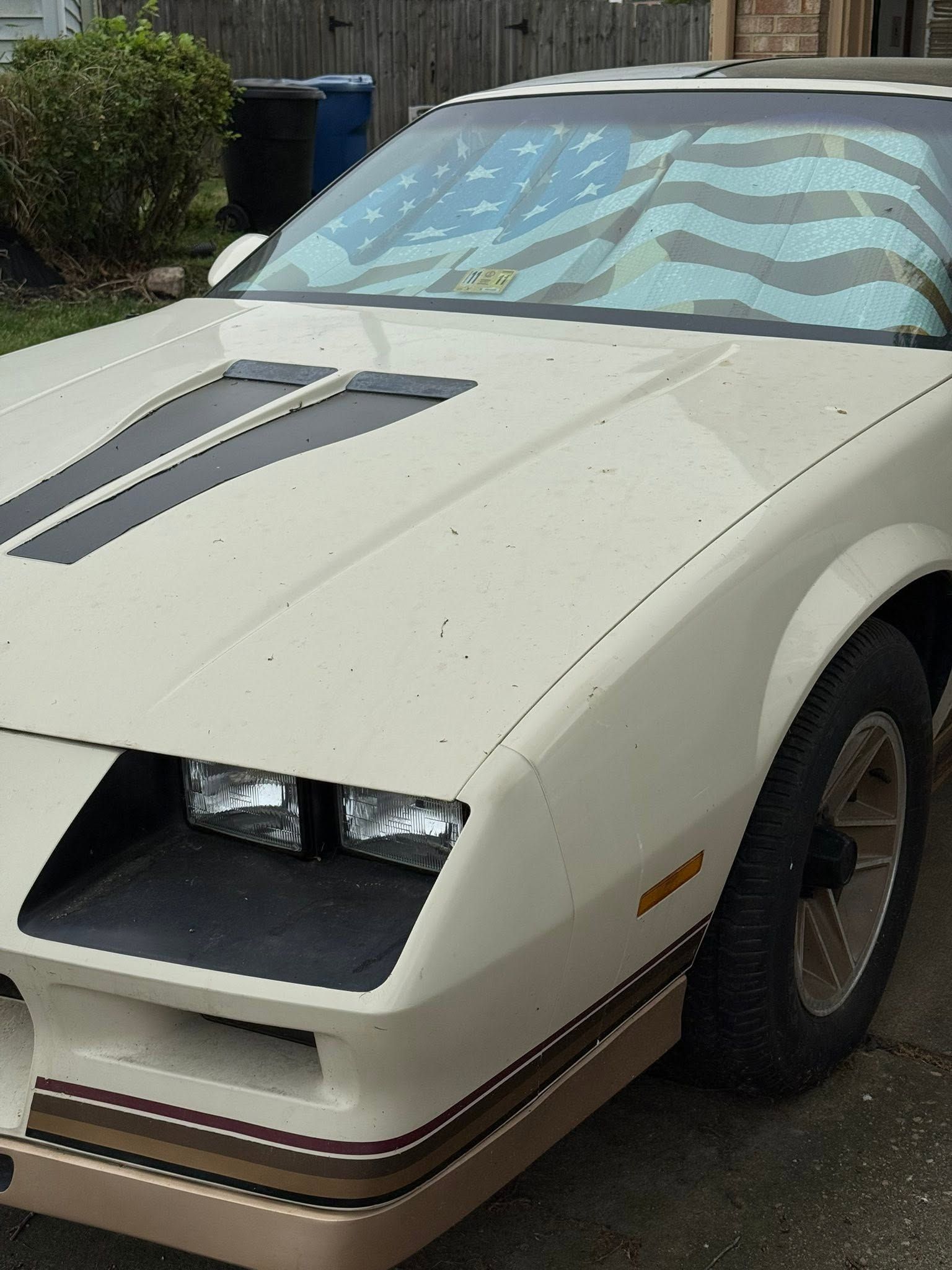 Cream-colored sports car with pop-up headlights parked on a driveway, front view.