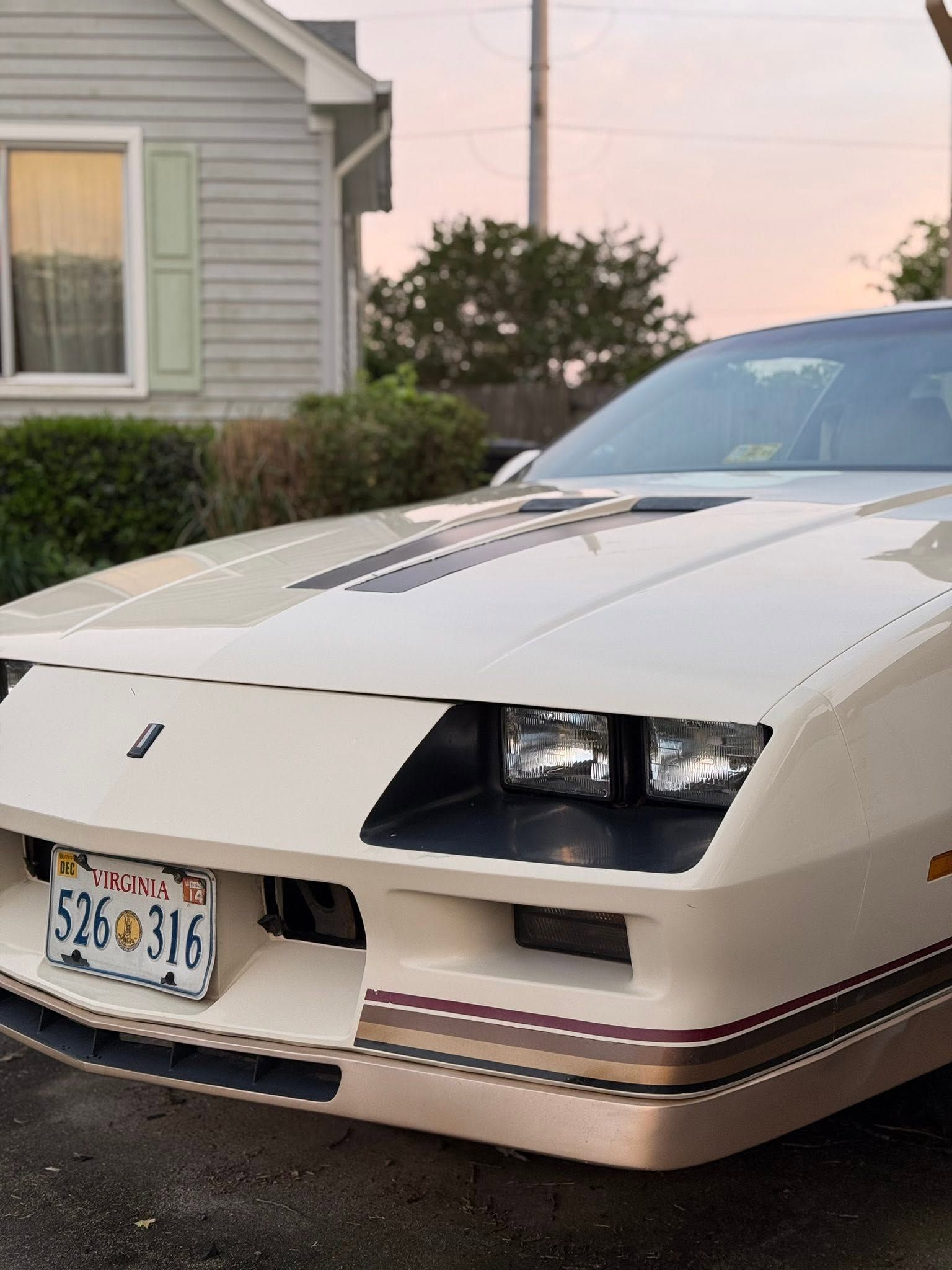 Beige sports car parked in a driveway beside a house at dusk