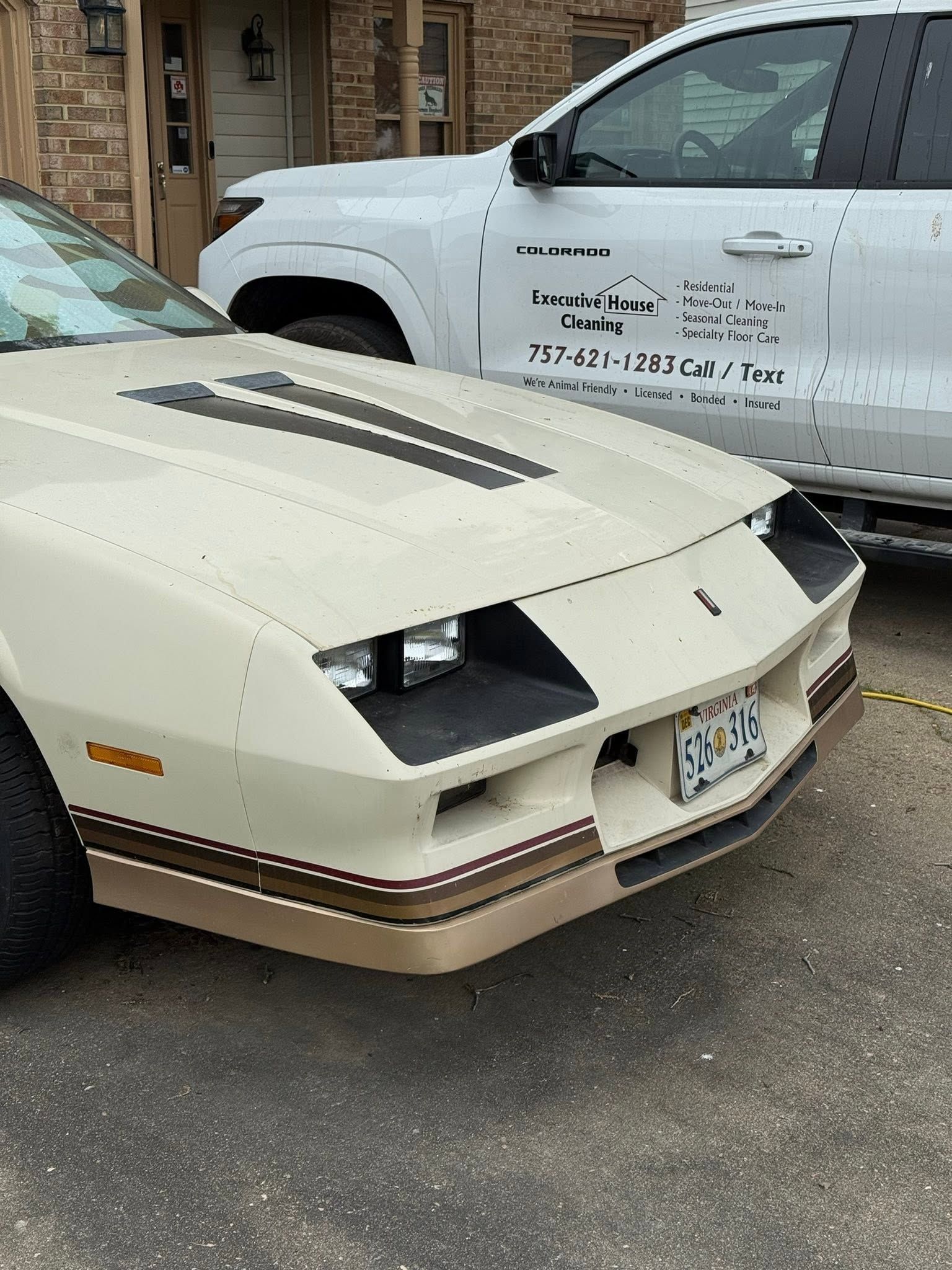 Beige vintage sports car parked beside a white pickup truck on a street.
