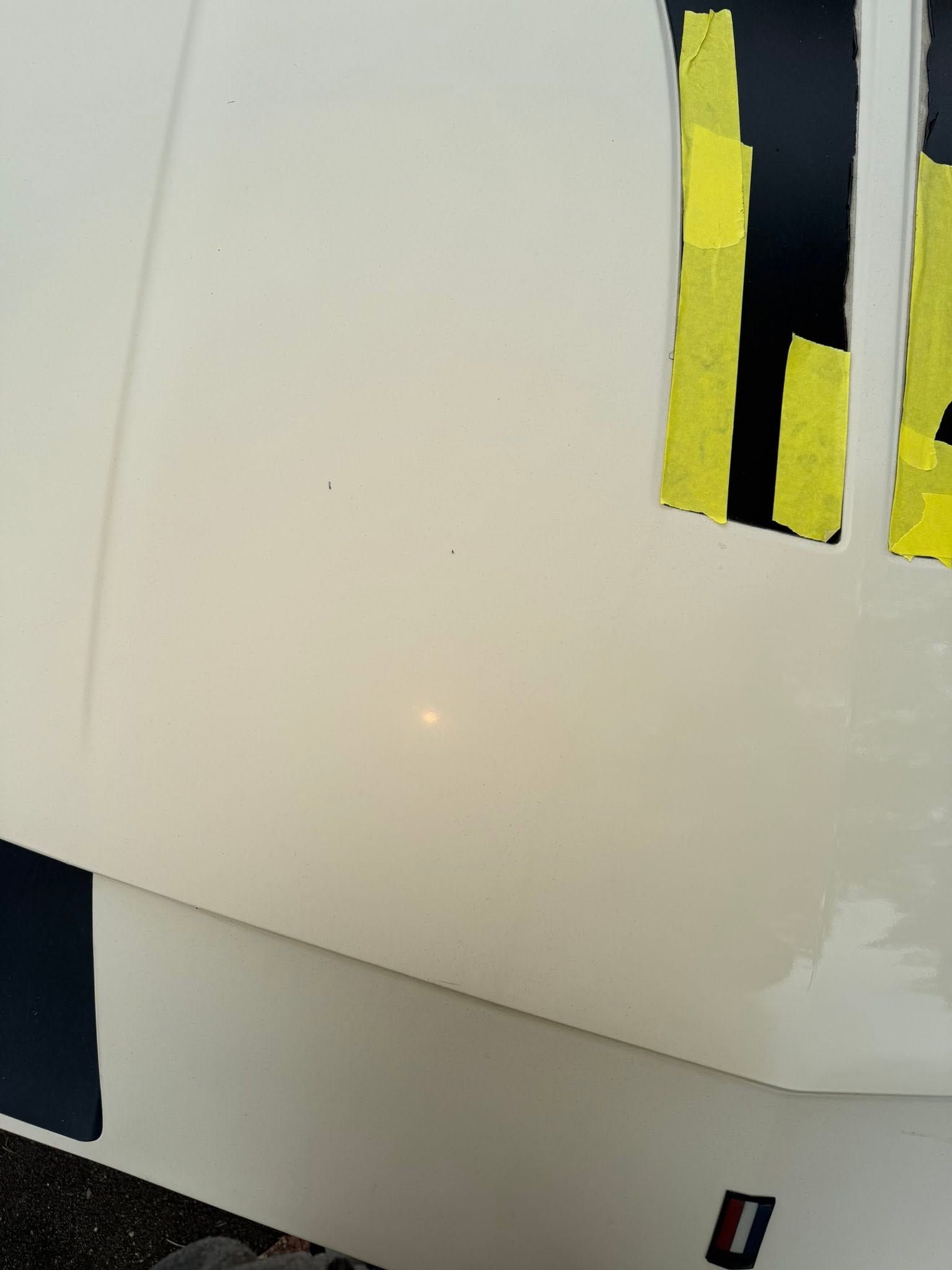 White car body panel with yellow-striped vents and a small black-and-red emblem near the bottom.
