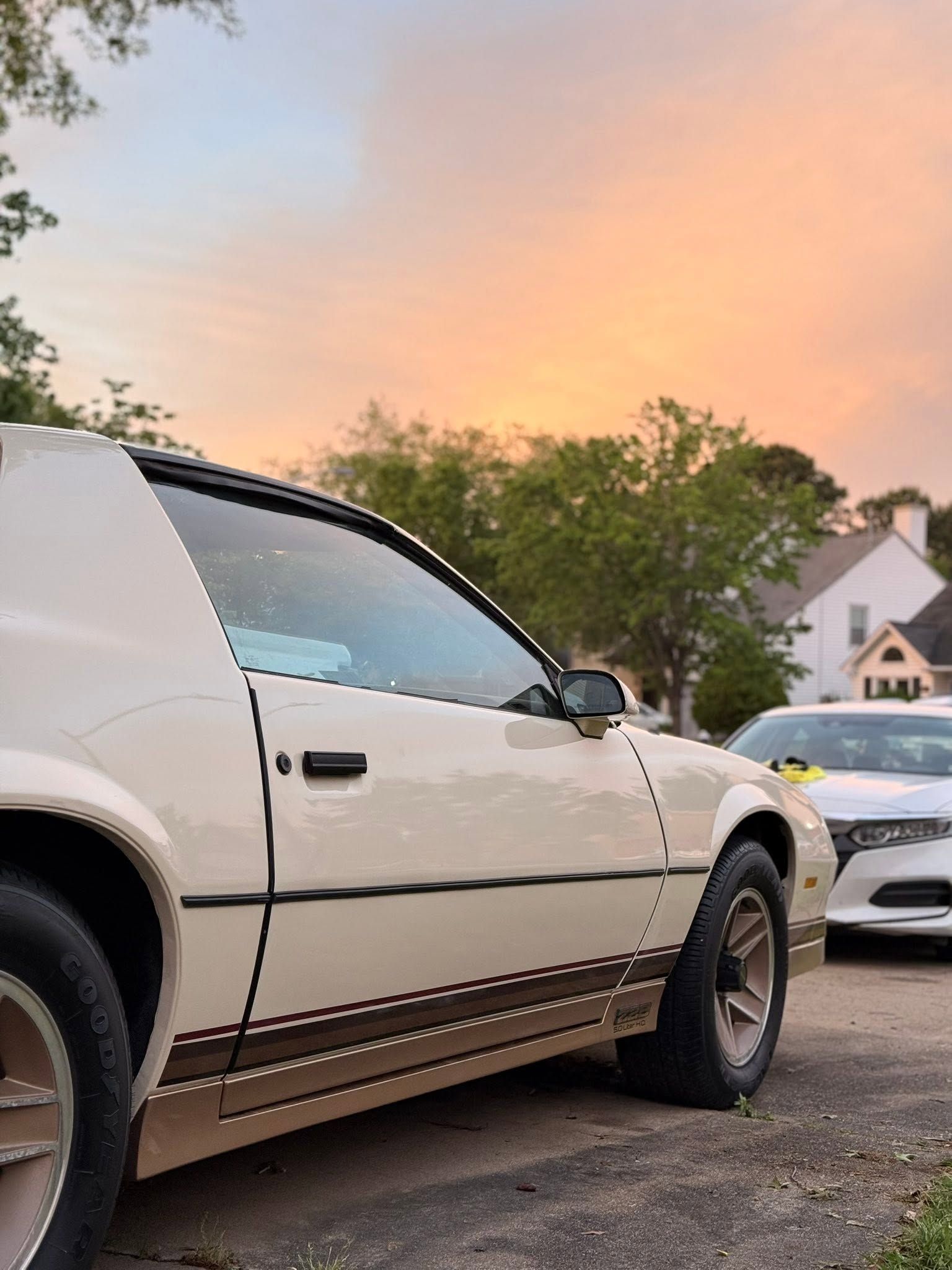 White SUV parked on a driveway at sunset, with houses and trees in the background.