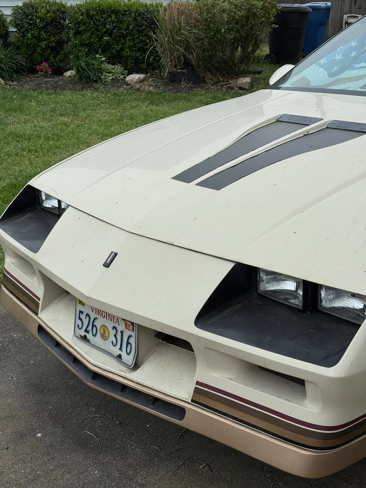 Front view of a beige sports car with pop-up headlights and a Florida license plate parked in a driveway