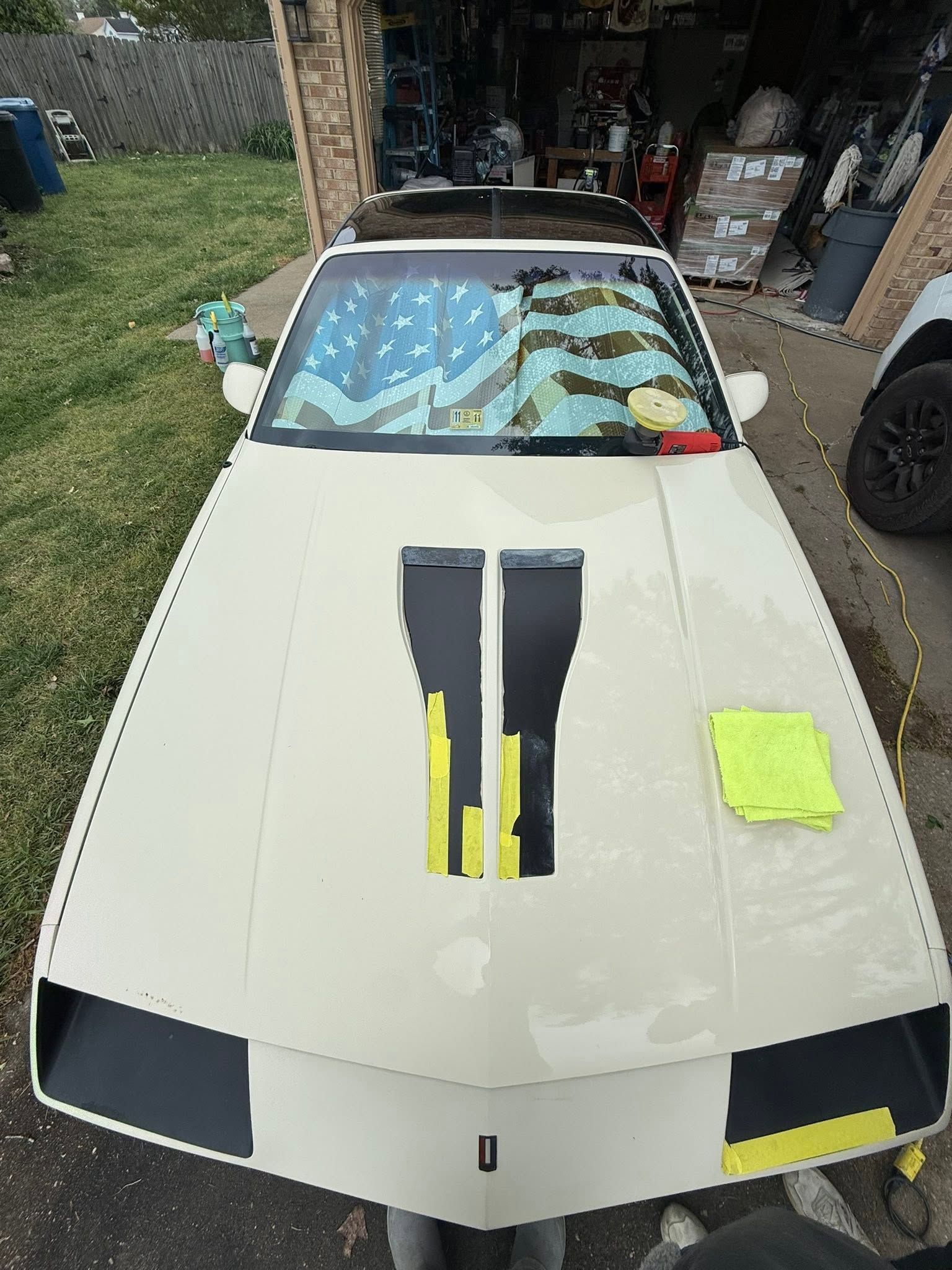 White sports car with black hood stripes and yellow accents parked in a driveway.