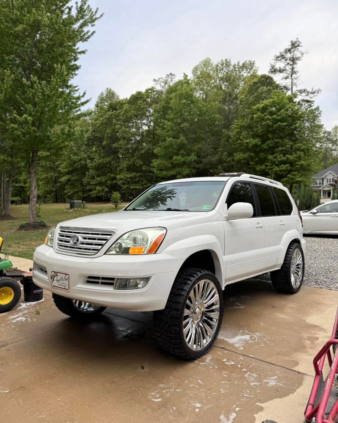 White SUV parked on a wet driveway with trees and a house in the background