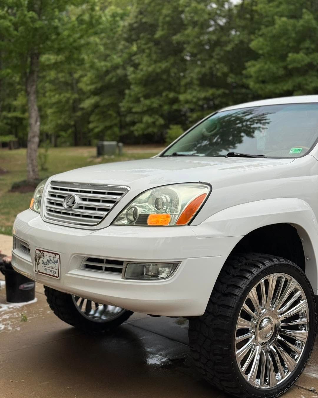 White SUV parked outdoors on a wet driveway, front view with chrome grille and large custom wheels
