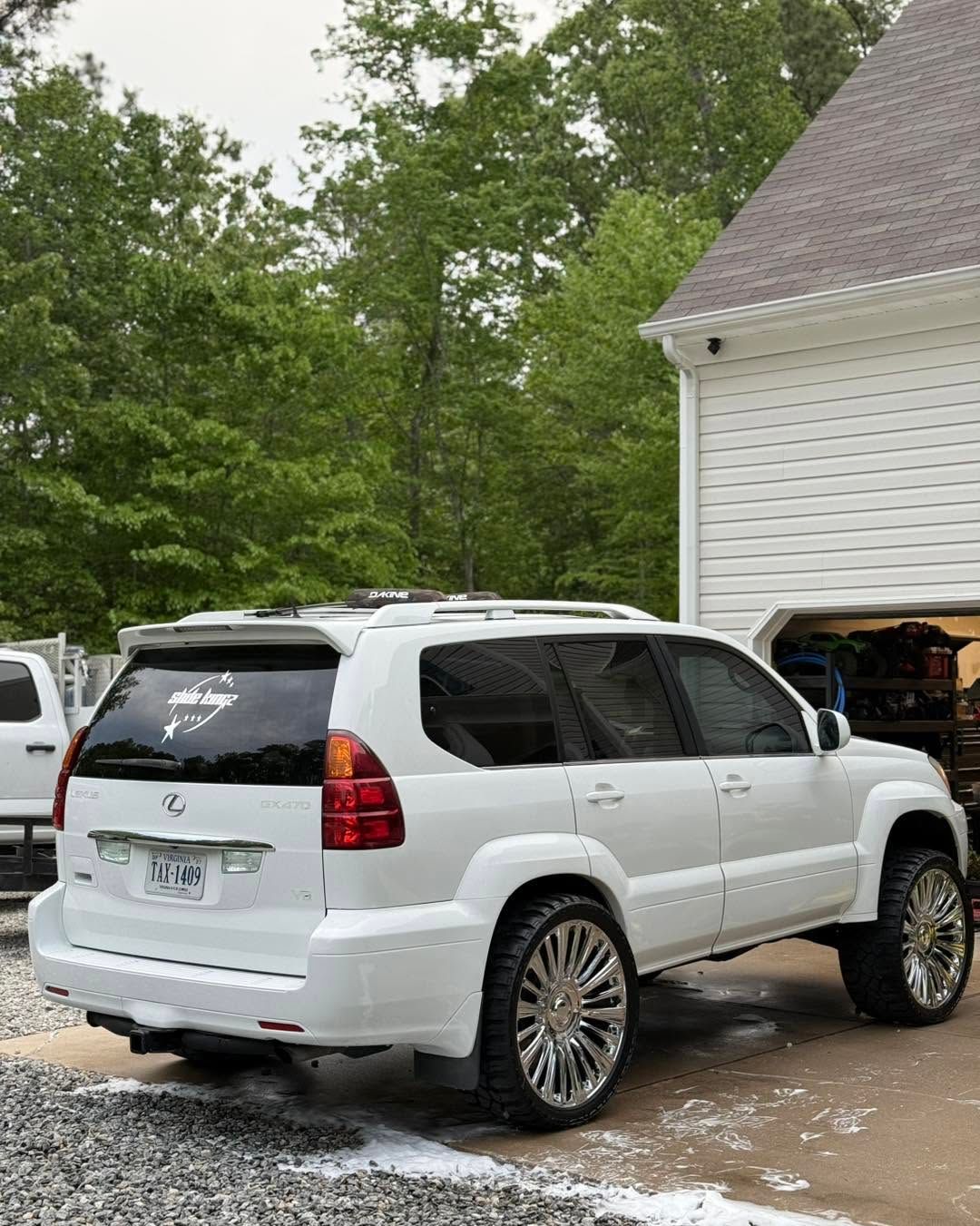 White SUV parked beside a house with trees in the background