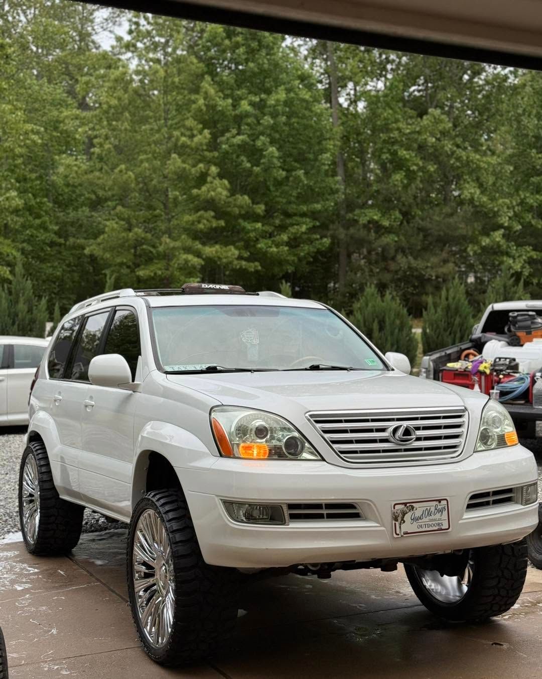 White SUV with chrome grille and large wheels parked on a wet road beside trees