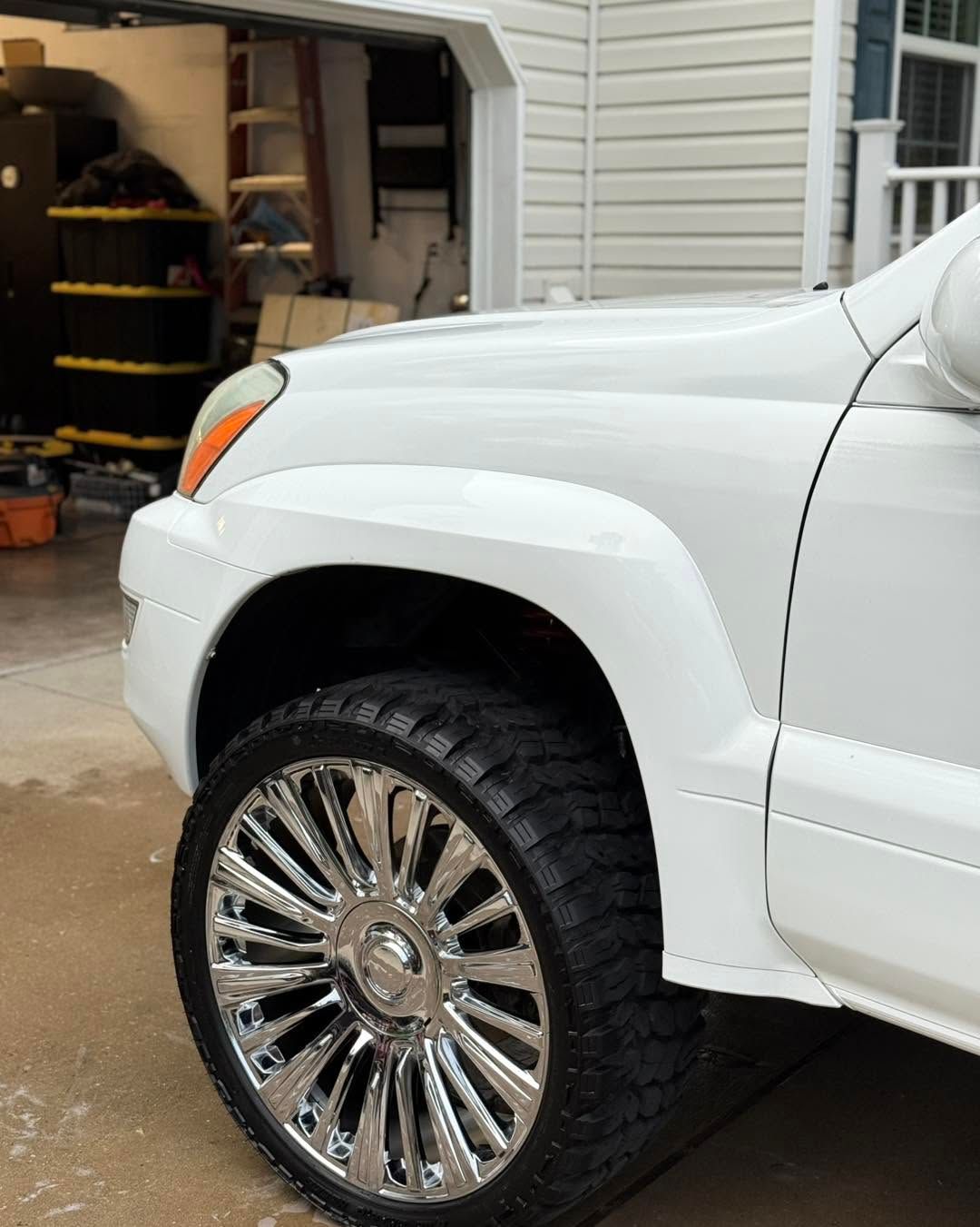 White SUV with chrome wheel parked in a driveway near an open garage