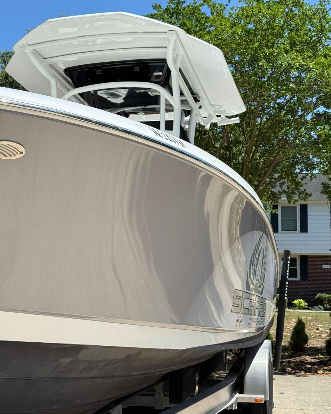 Large white boat with a T-top parked outdoors beside a house and trees