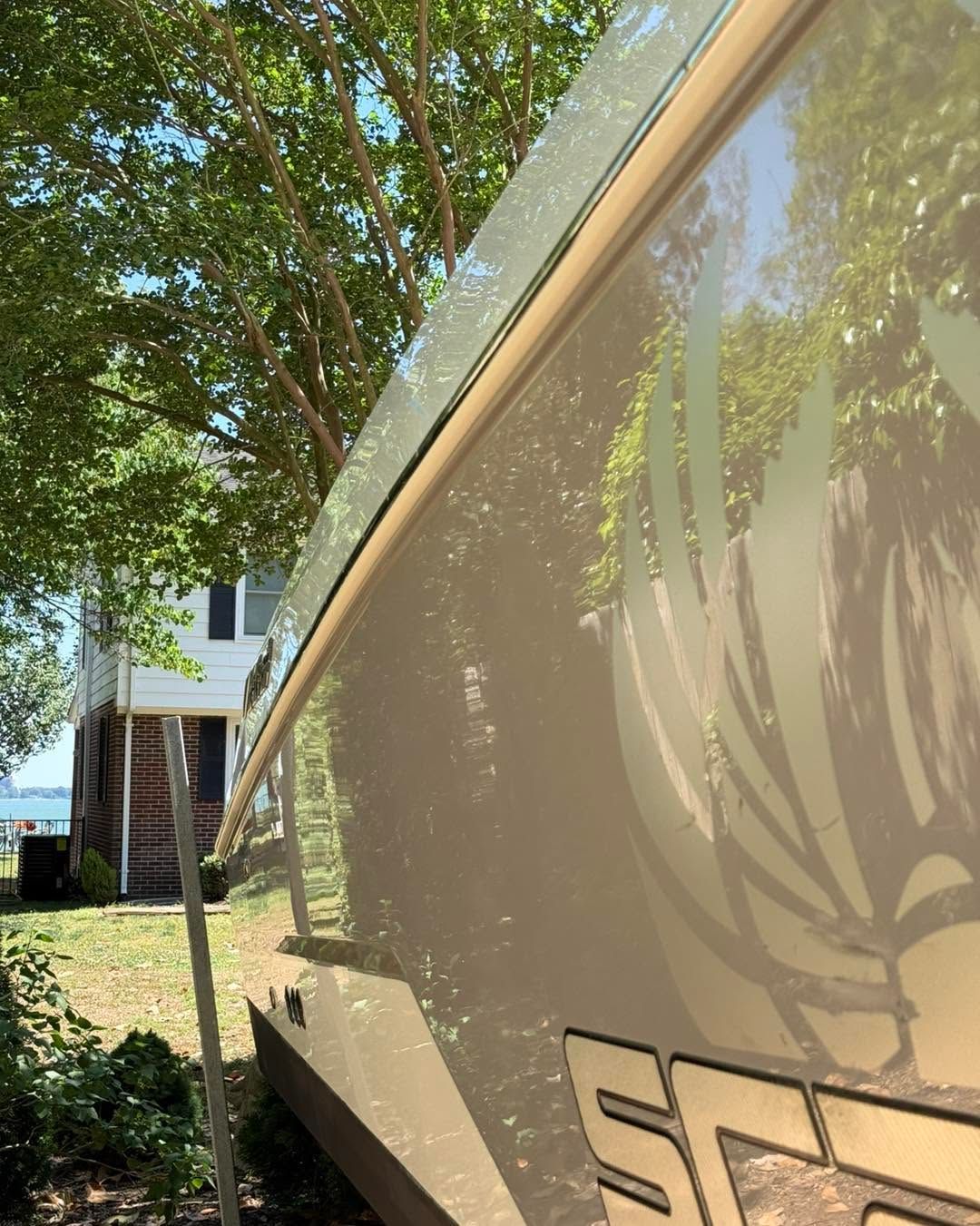 Side view of a white RV with beige trim parked beside trees and a building in daylight