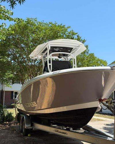 Large tan center-console boat on a trailer in a driveway, with a white T-top and blue sky overhead