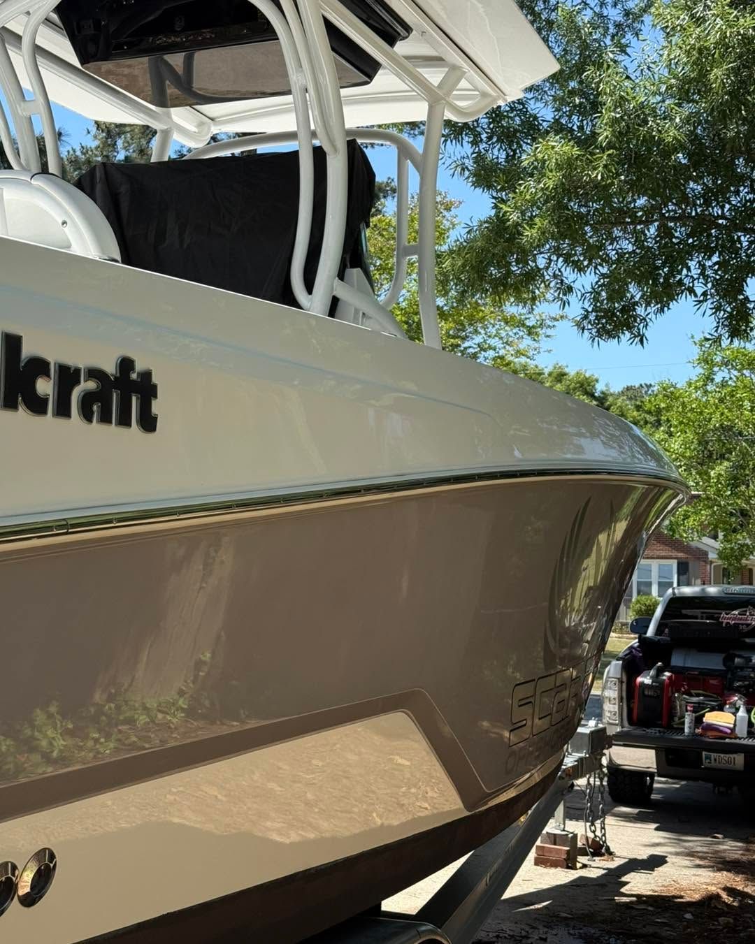 White center-console boat on a trailer parked in a driveway under trees.