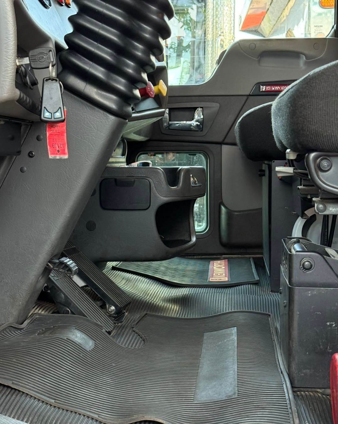 Interior of a heavy vehicle cab with black seats, textured floor, and control panel beside the passenger seat