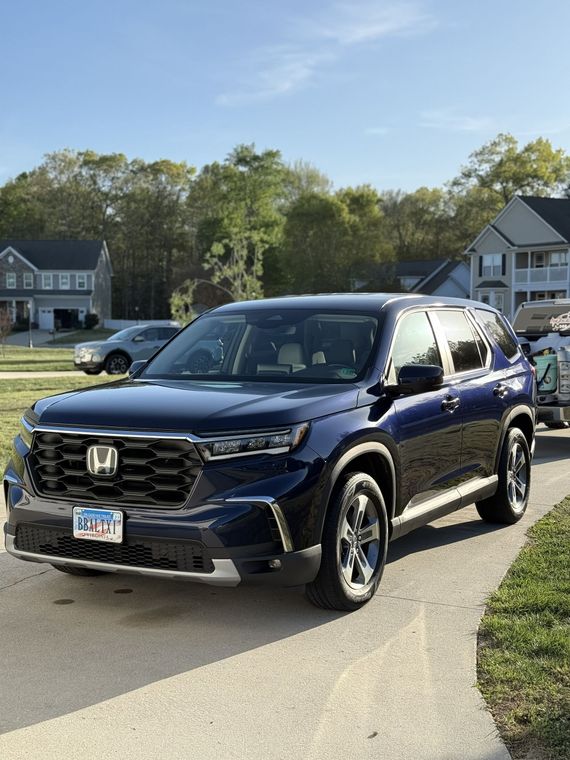 Blue Honda SUV parked in a suburban driveway with houses and trees in the background