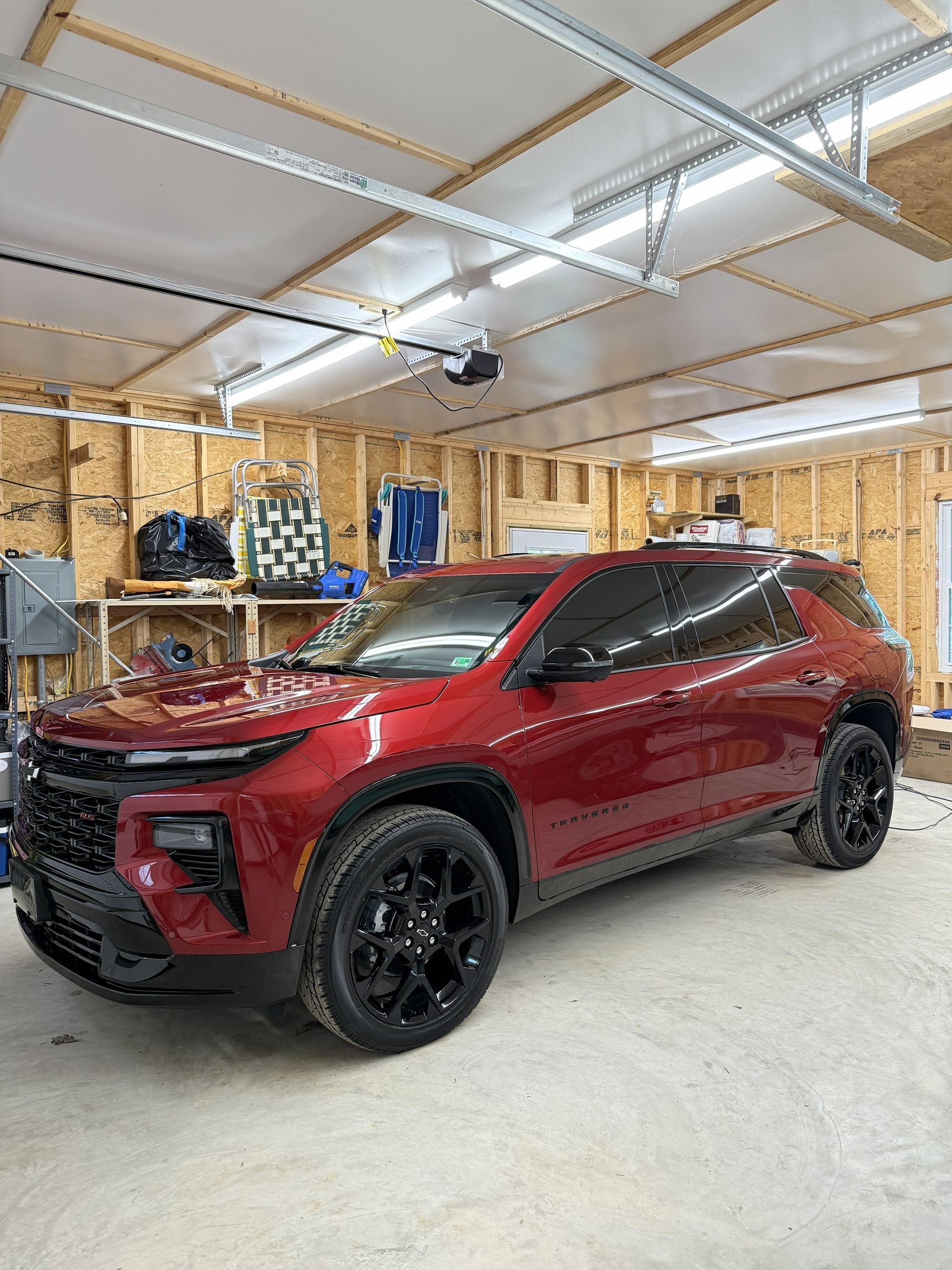 Red SUV parked inside a garage with unfinished wooden walls and ceiling lights.