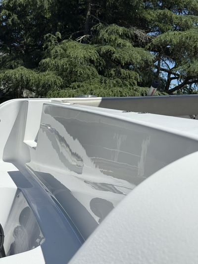 Close-up of a white boat hull with gray interior, against green trees and blue sky