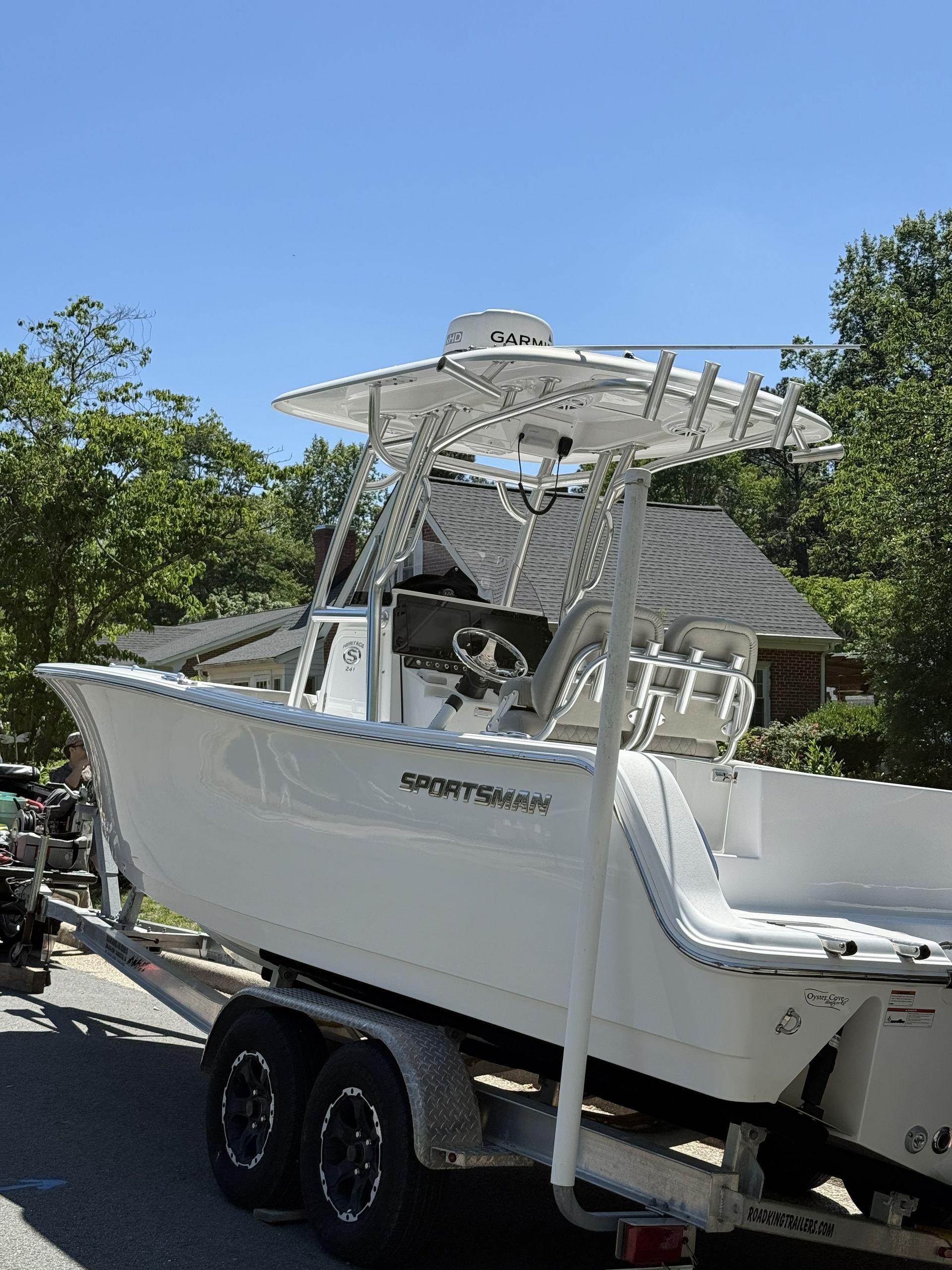 White motorboat on a trailer with a canopy, parked outdoors under a blue sky.
