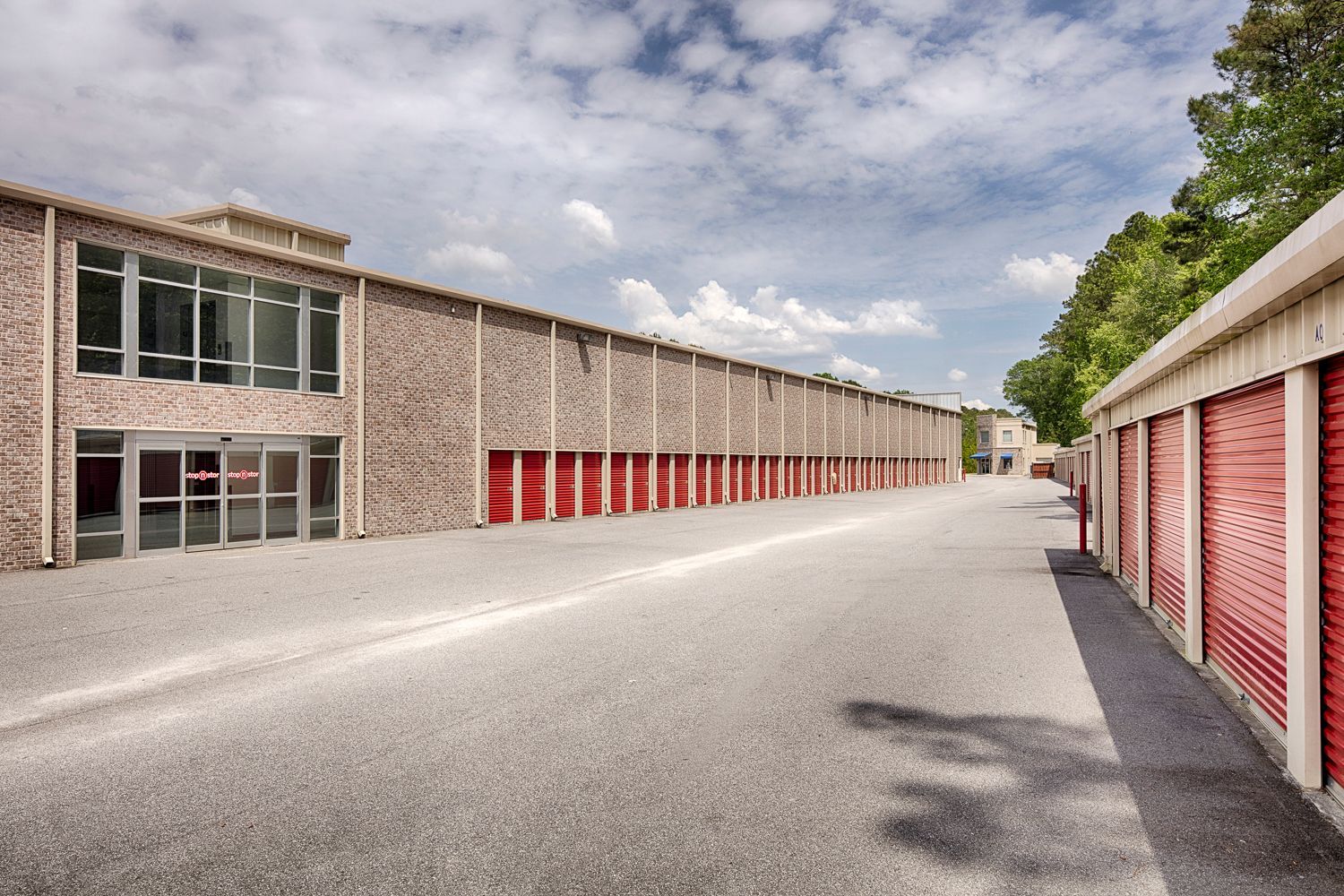 Outdoor storage units with wide drive aisles and red roll-up doors at Stop N Stor