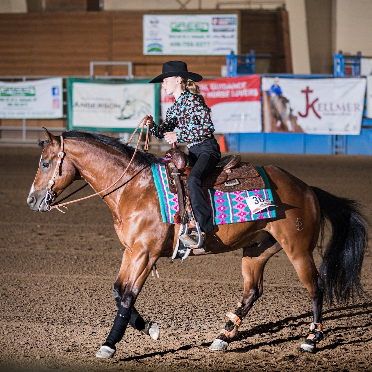 A woman is riding a brown horse in a rodeo arena
