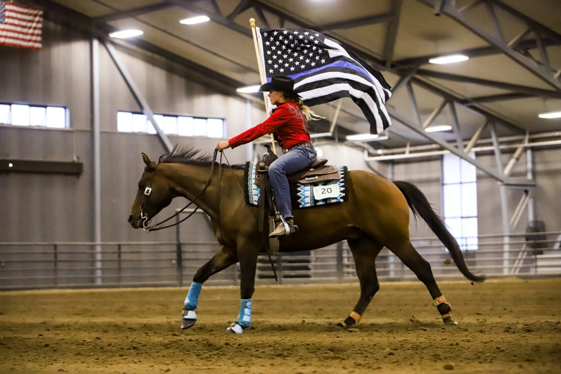 A woman is riding a horse while holding an american flag.