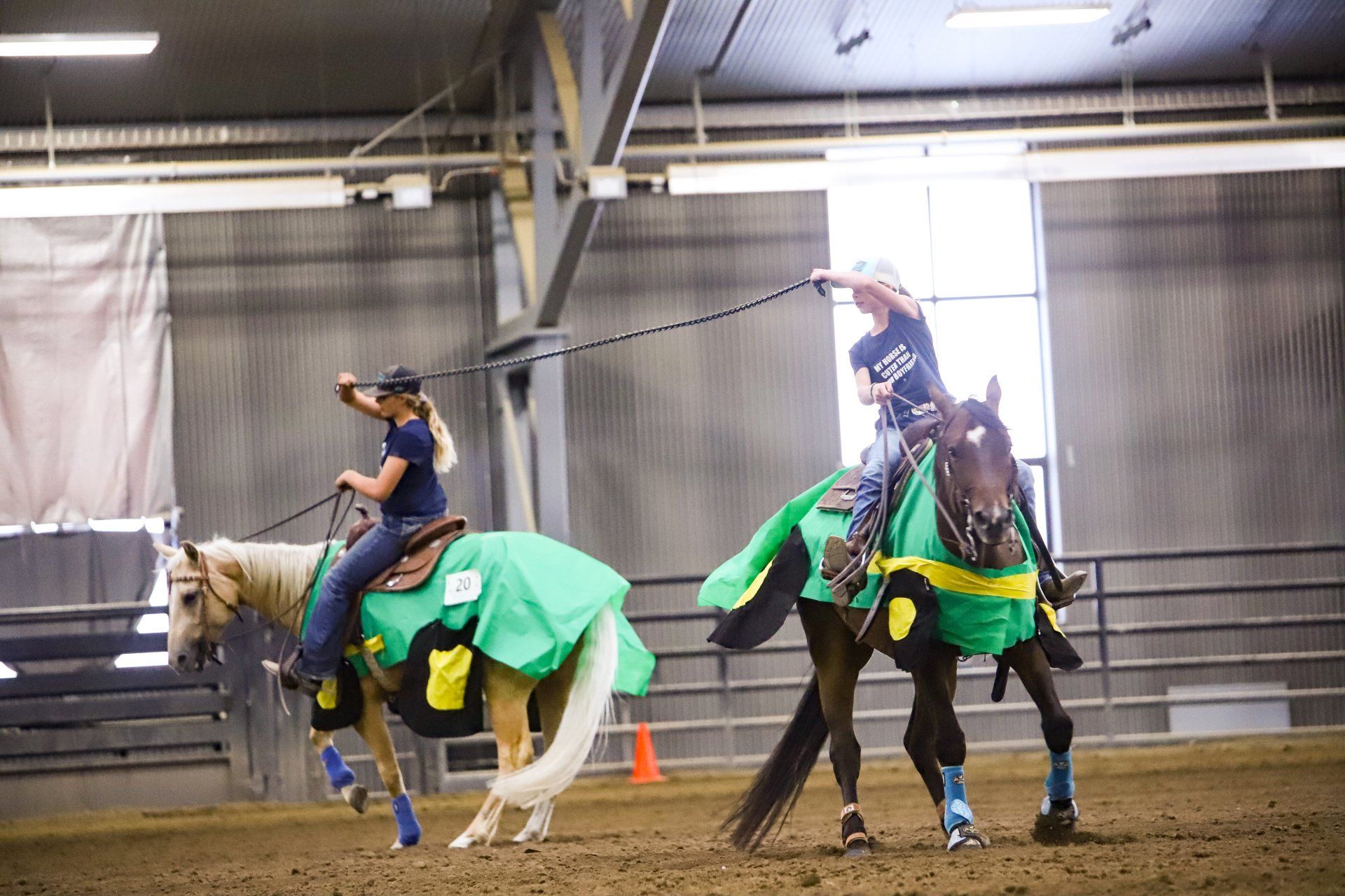 Two people are riding horses in an indoor arena.