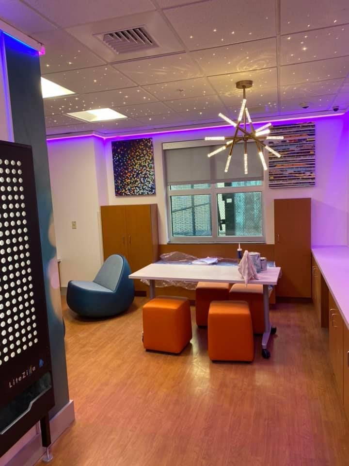 Room with orange accents, art, and starry ceiling lighting. A desk, seating, and windows are visible.