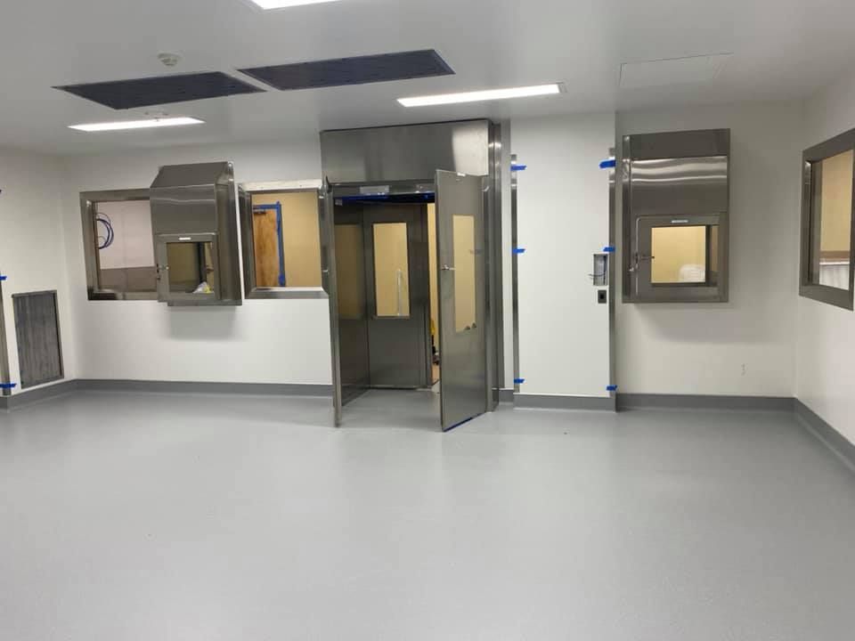 Clean room with gray floor, white walls, stainless steel doors and windows.