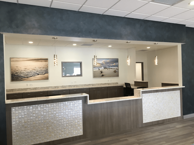 Reception area with gray, white, and wood-tone desk, artwork, pendant lights, and blue-gray wall accent.