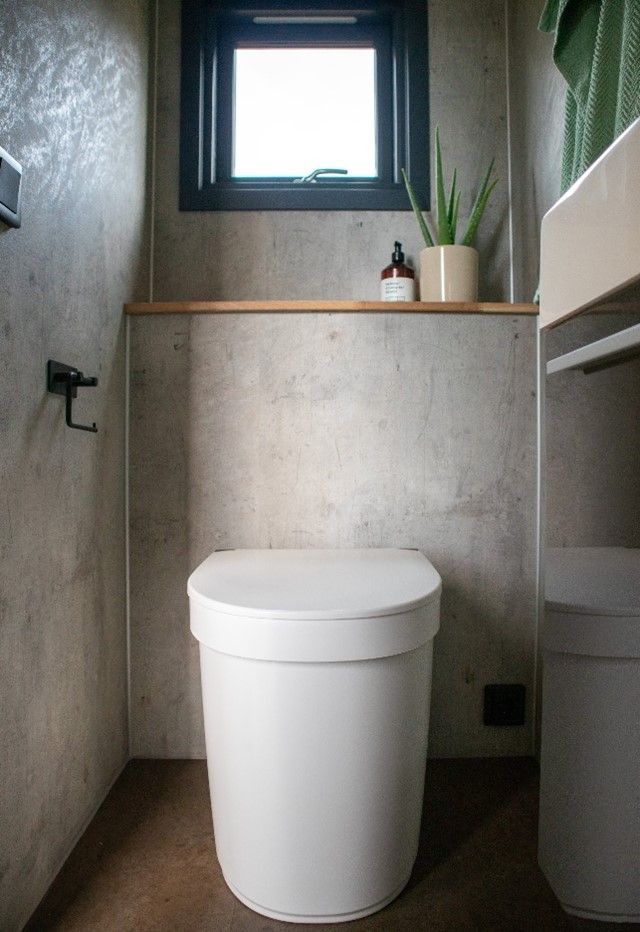 Et hvidt toilet på et badeværelse ved siden af et vindue.