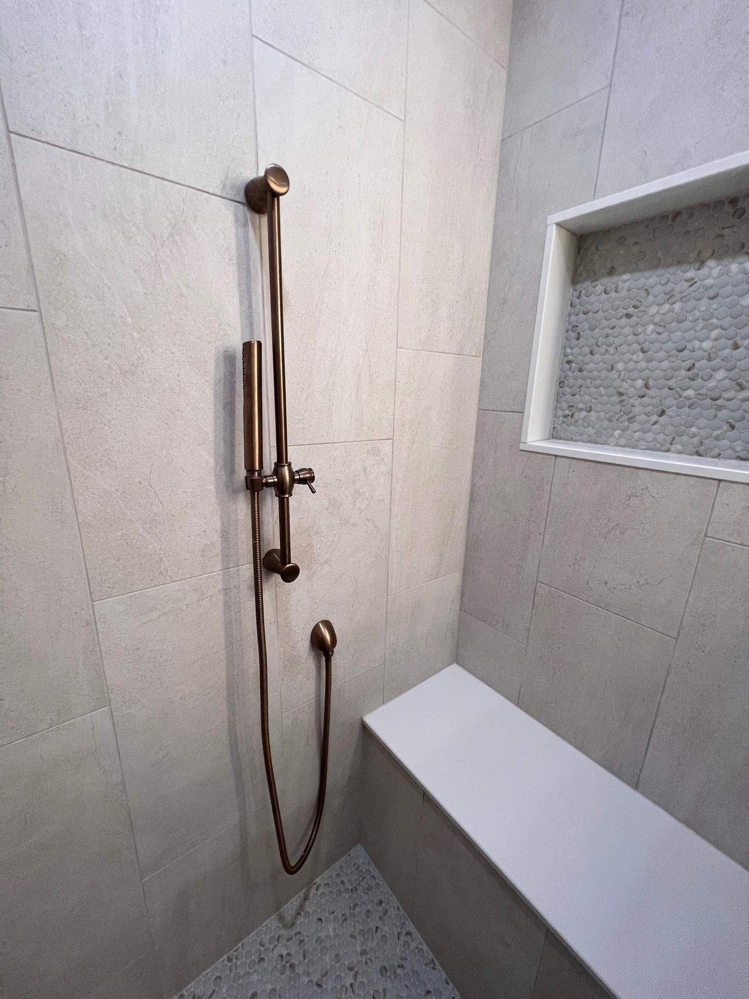 Shower stall with bronze fixtures, light gray tile walls, and a white bench.