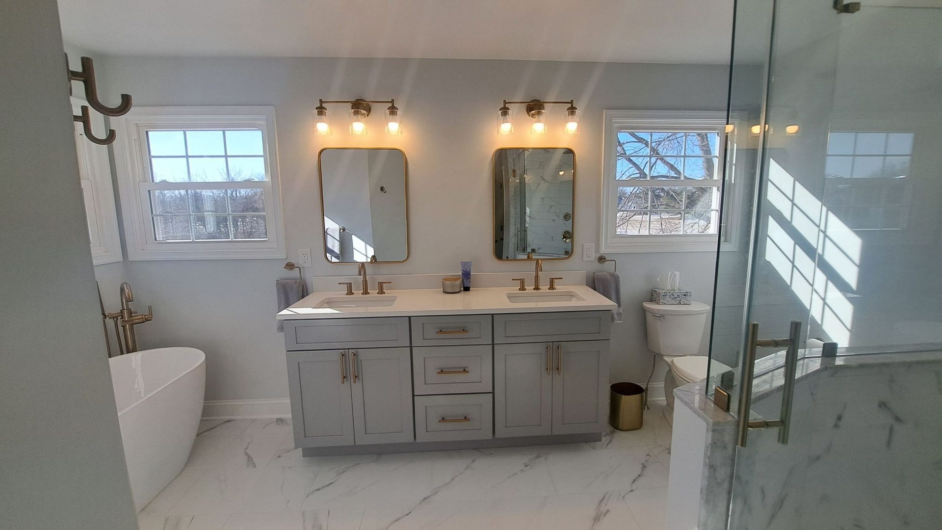 Modern bathroom with dark green vanity, gold fixtures, large mirror, and shower with decorative screen.
