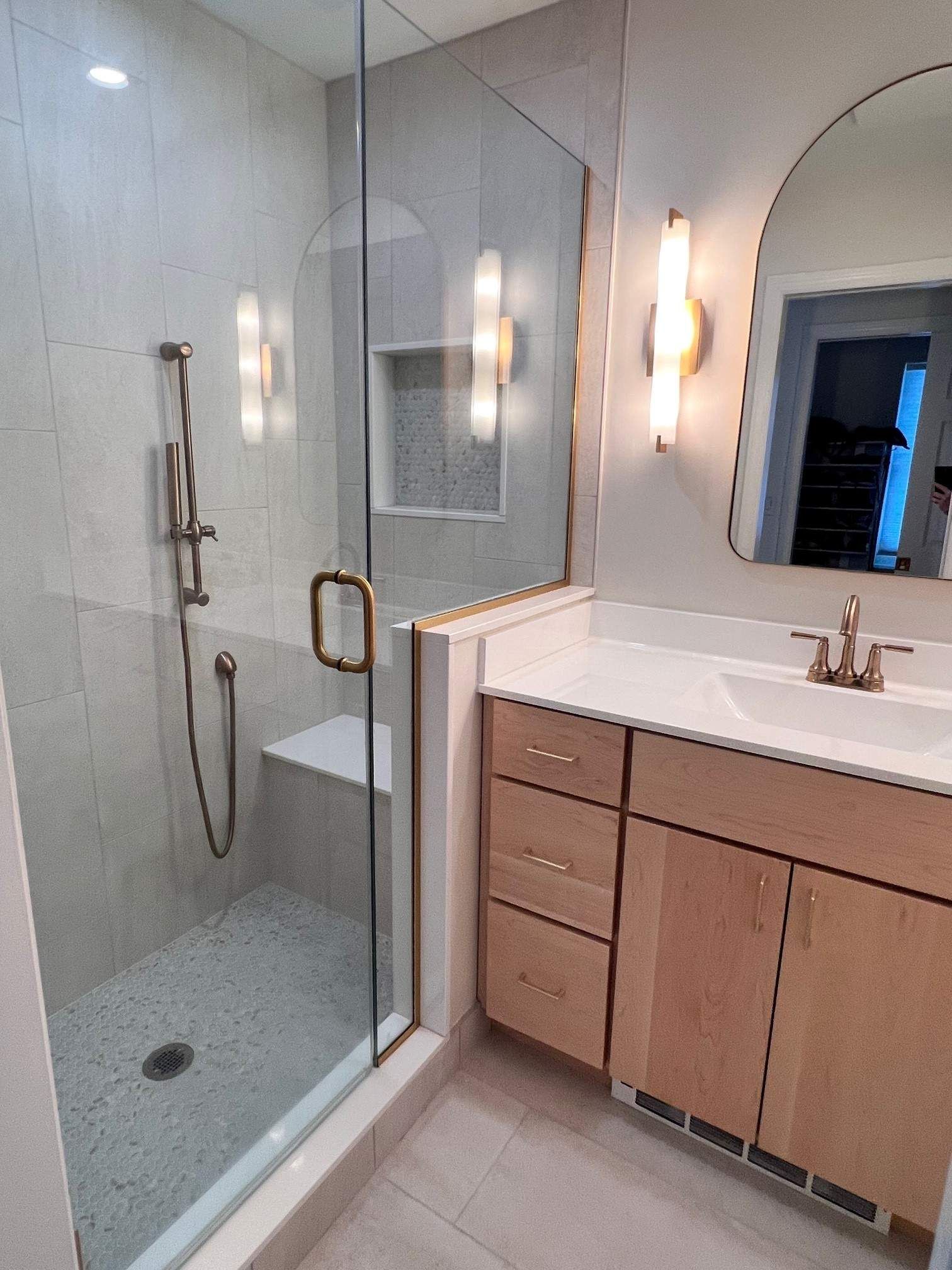 Modern bathroom with a glass-enclosed shower, gold hardware, light wood vanity, and a large mirror.