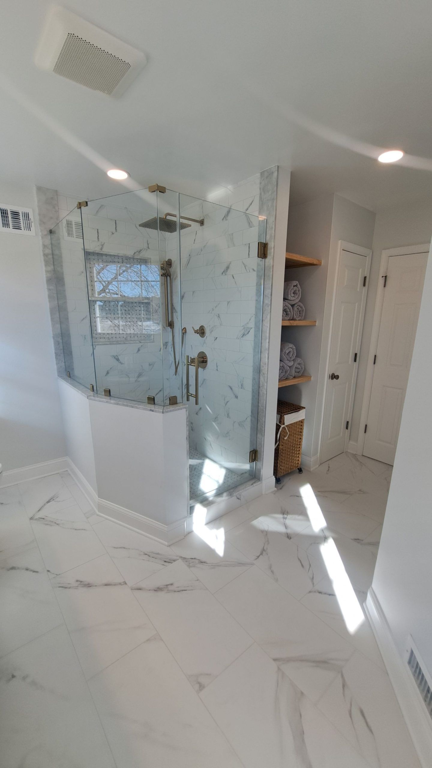 Newly remodeled bathroom with marble-look tile, glass shower, and wooden shelves.