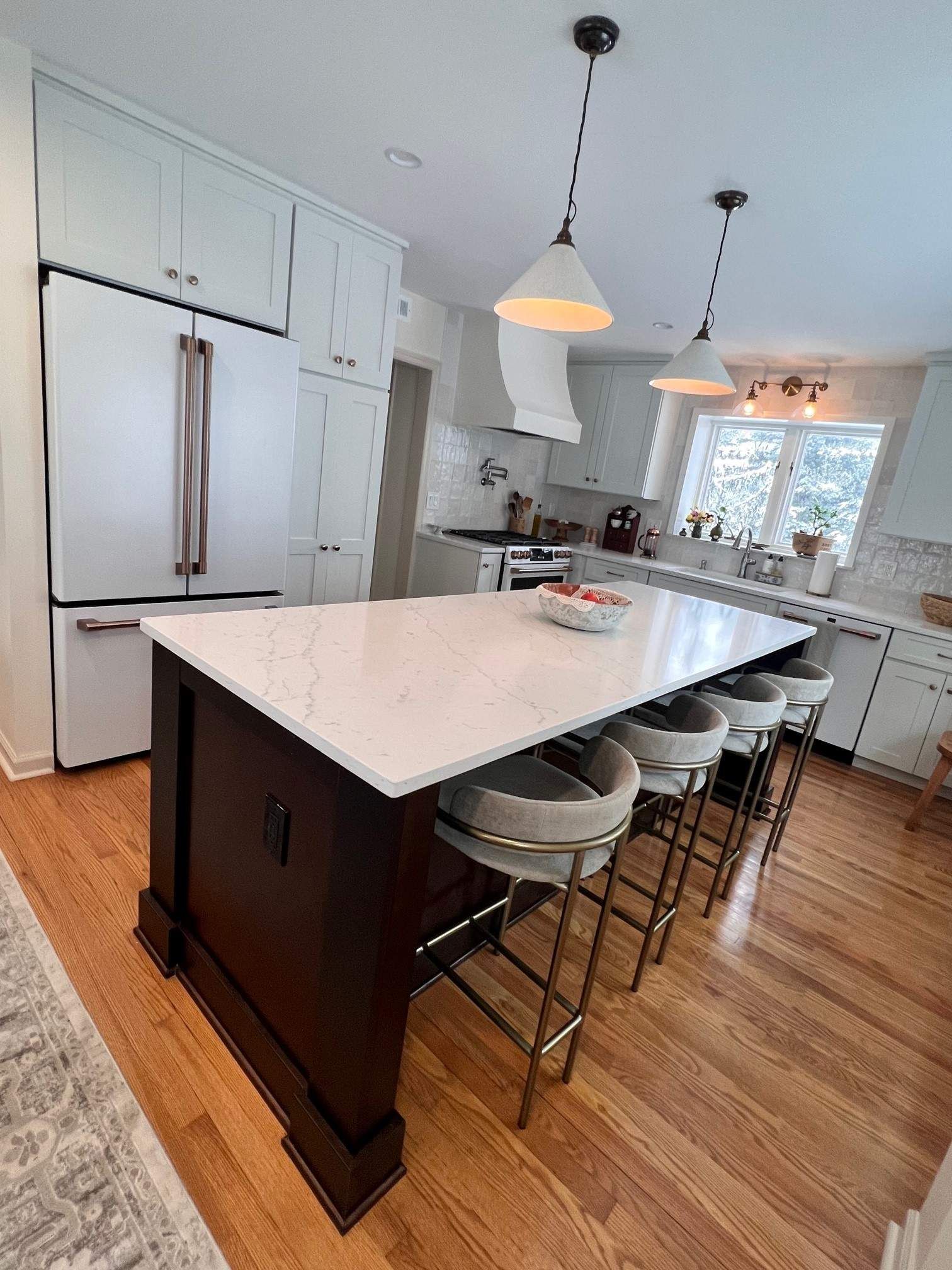Kitchen island with white countertop, dark wood base, and three gray bar stools.