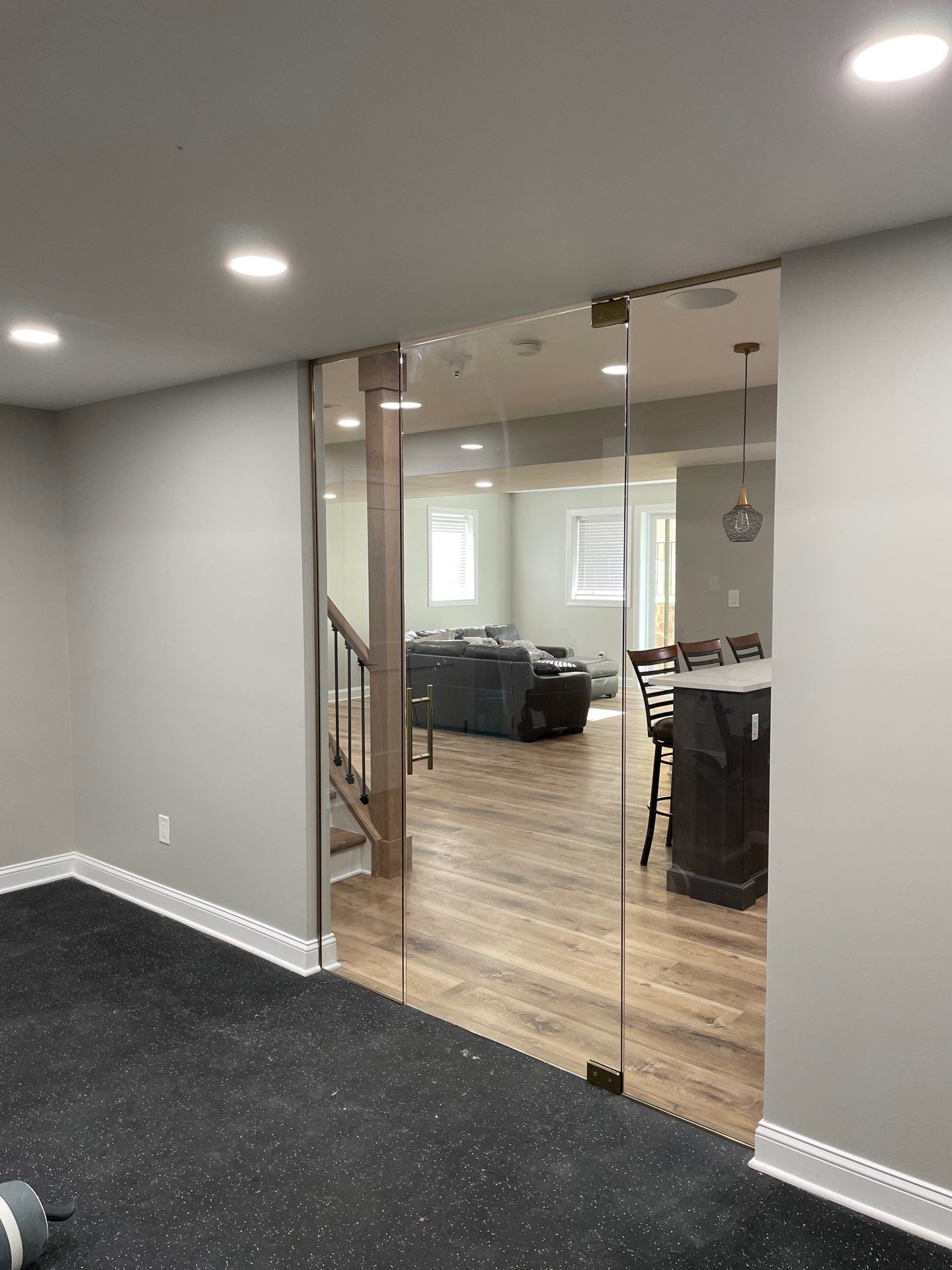Basement with glass doors, leading to a living area with hardwood floors and stairs. Grey walls and rubber floor in the basement.