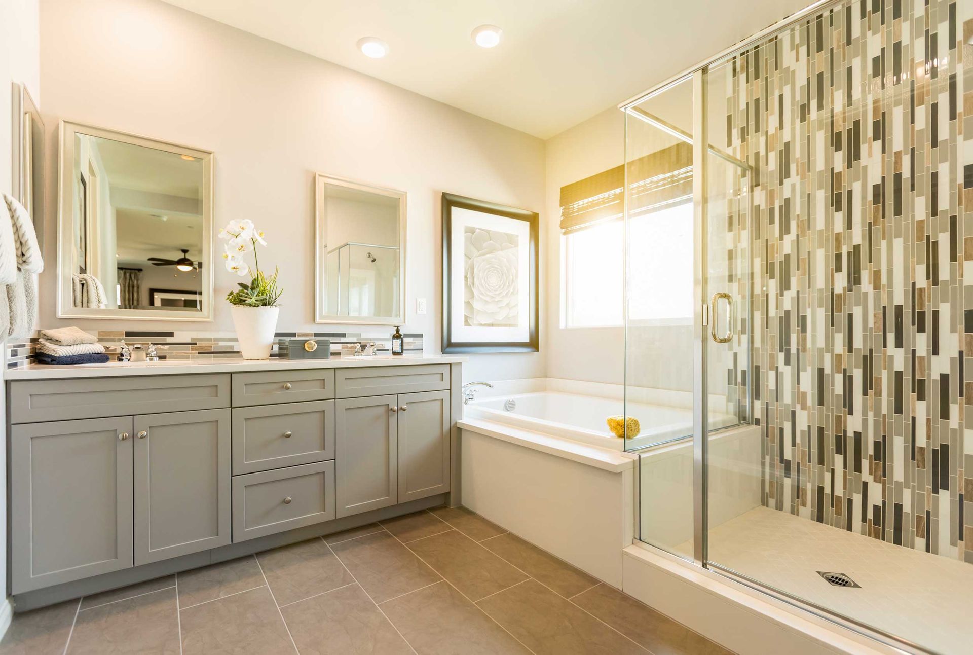 A bathroom with a double sink vanity, soaking tub, and glass shower with a patterned tile wall