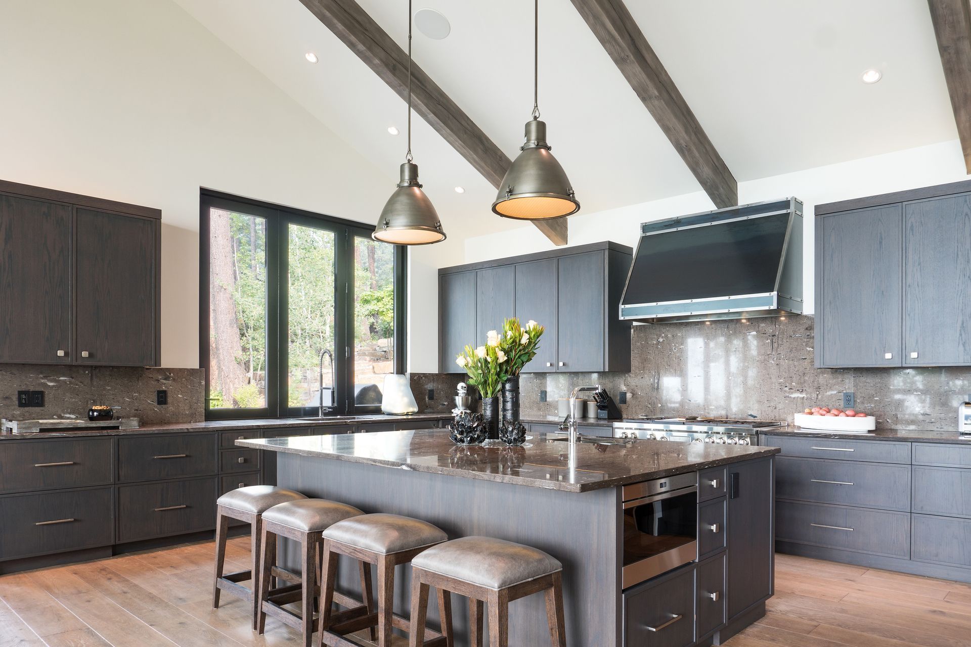A modern kitchen with an island with four stools and two pendant lights above.