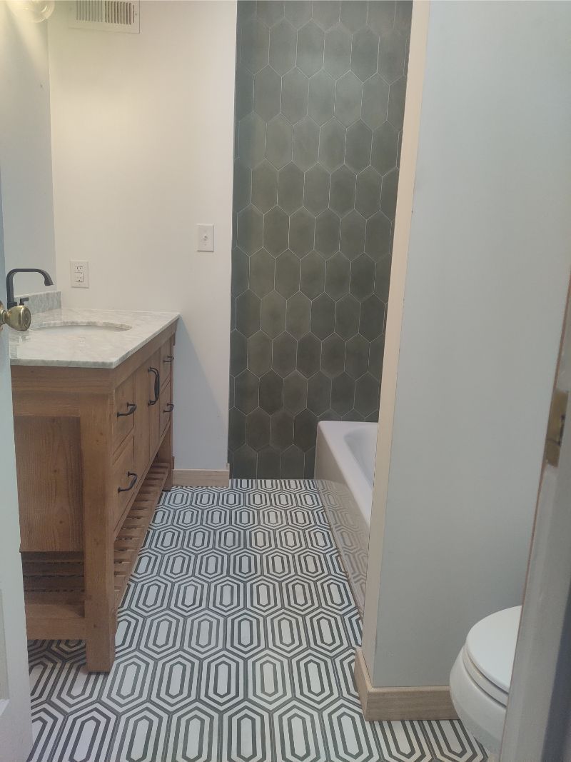 Bathroom with wood vanity, patterned floor, green tile wall, and a bathtub.