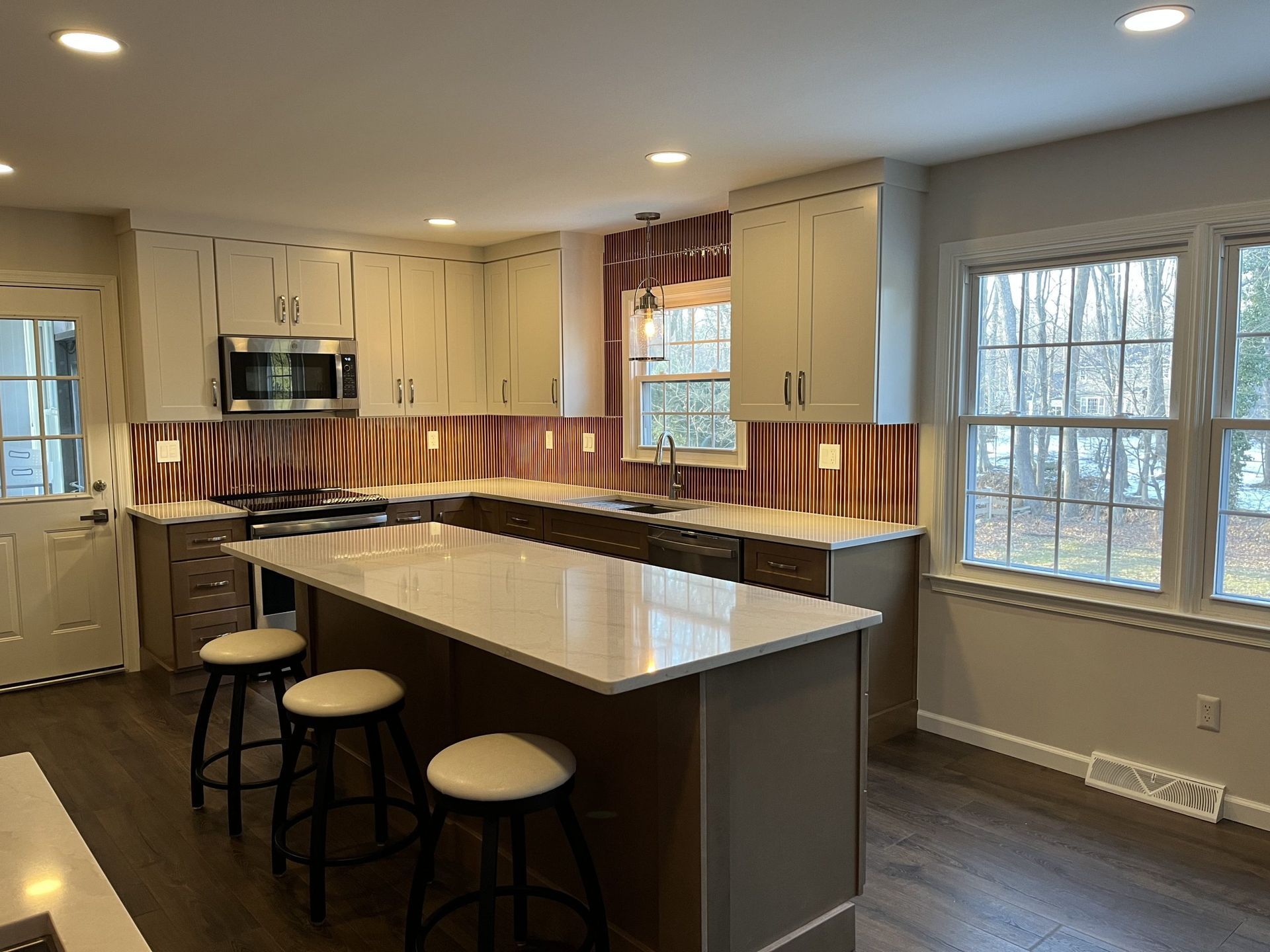Modern white kitchen with a large island, stainless steel appliances, and gold pendant lights.