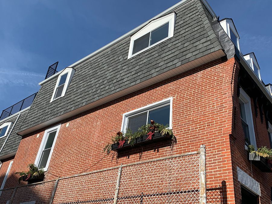 Red brick building with gray mansard roof, dormer windows, and window boxes with plants.