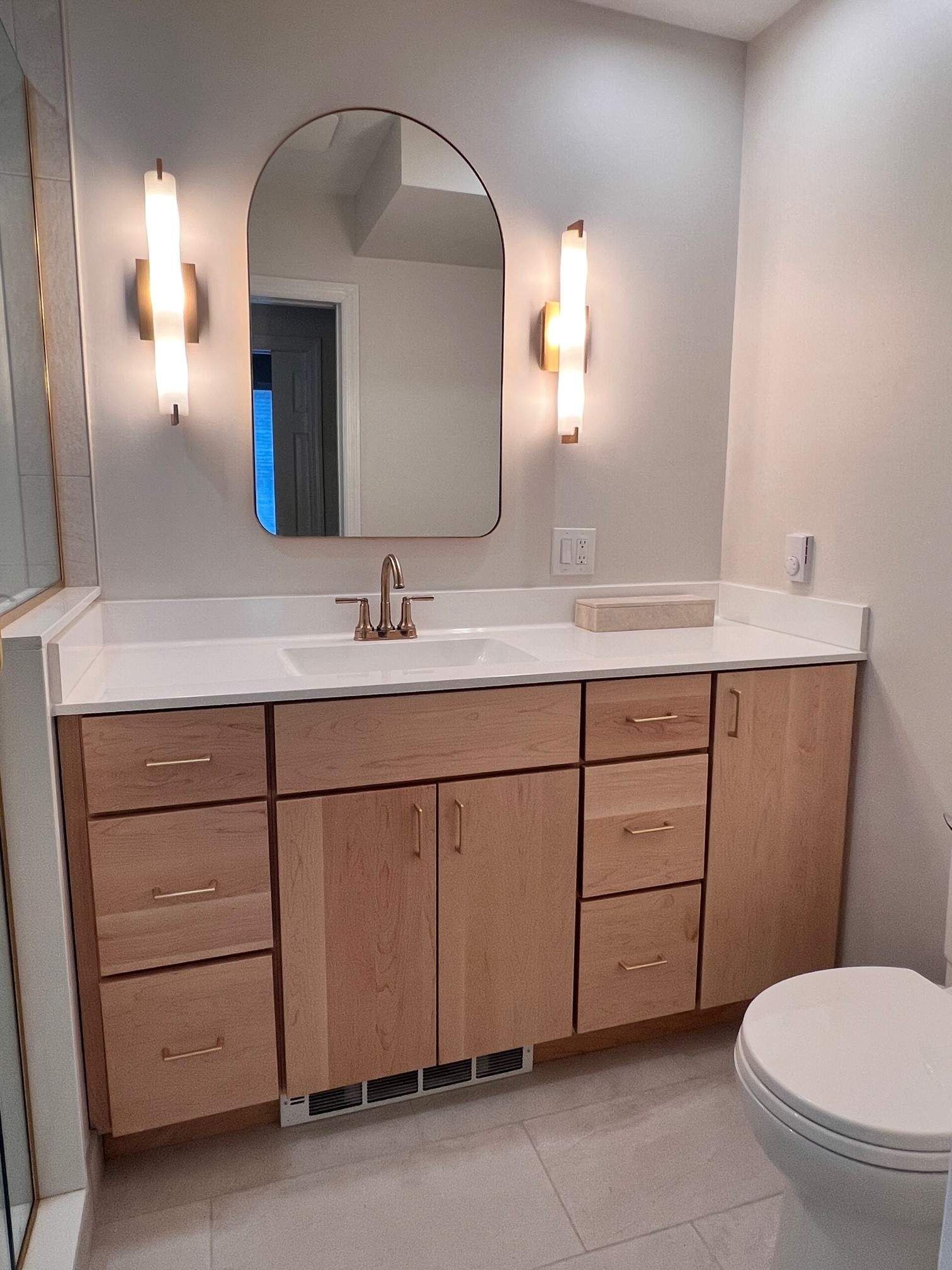 Bathroom with light wood vanity, white countertop, arched mirror, and sconces.