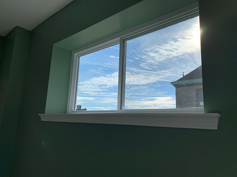 Green-walled room with a window showing a bright cloudy sky and part of a building.