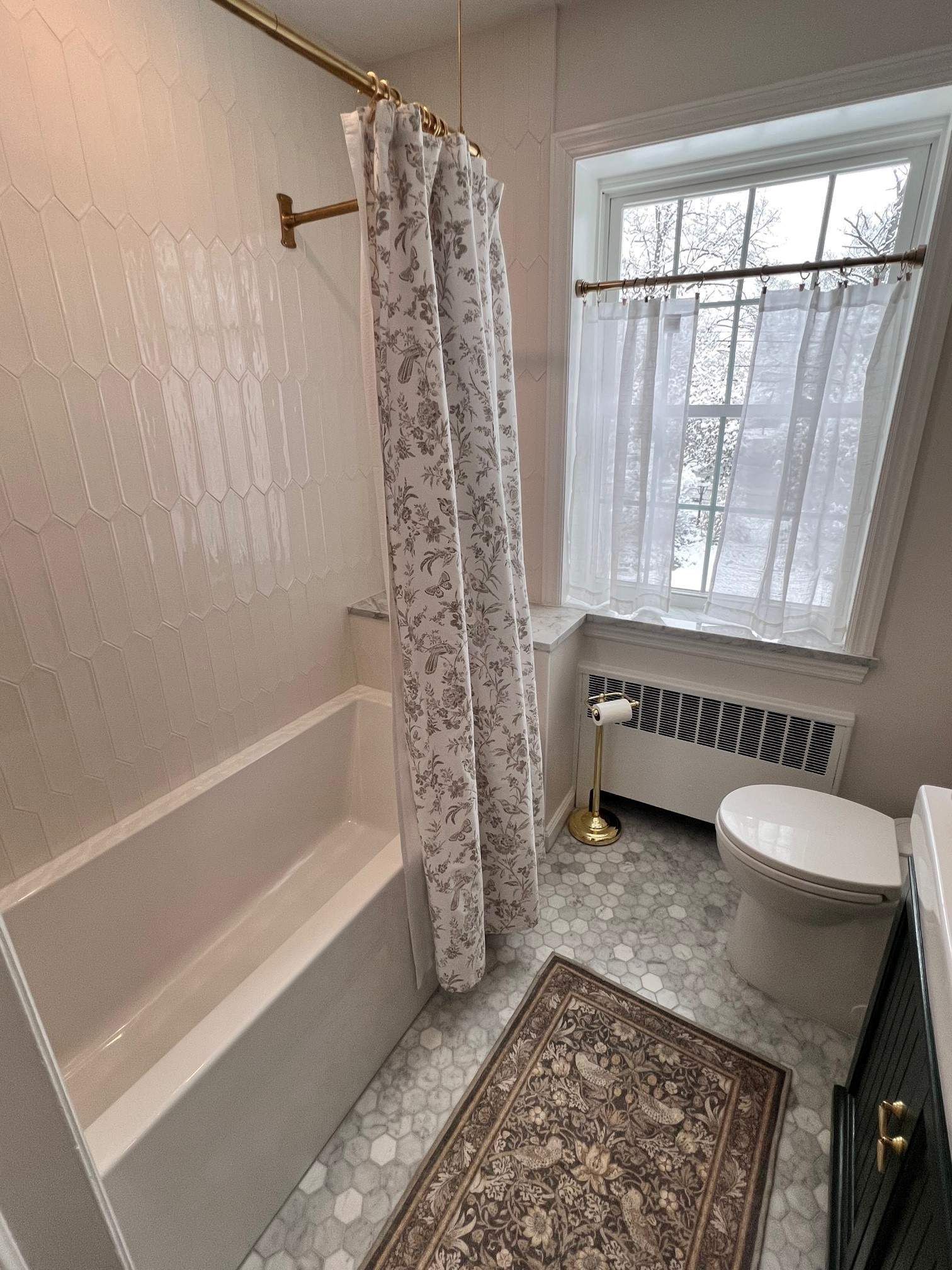 Bathroom with white tub, floral shower curtain, small window, and patterned tile floor.